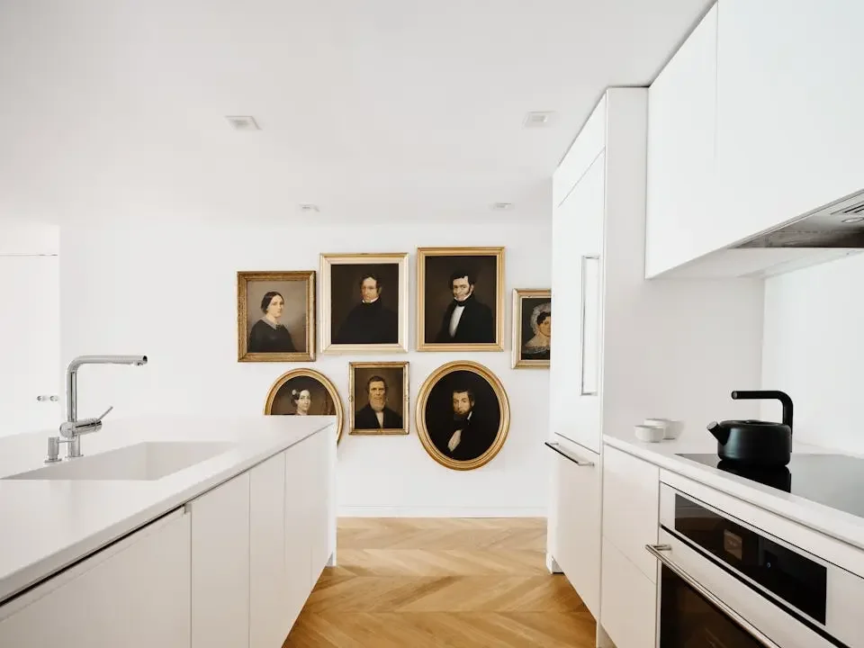 Modern white kitchen with framed classical portrait paintings on the wall
