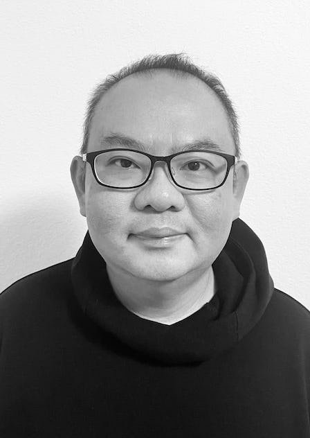 Black and white photo of a man wearing glasses and a hoodie, facing the camera with a neutral expression.
