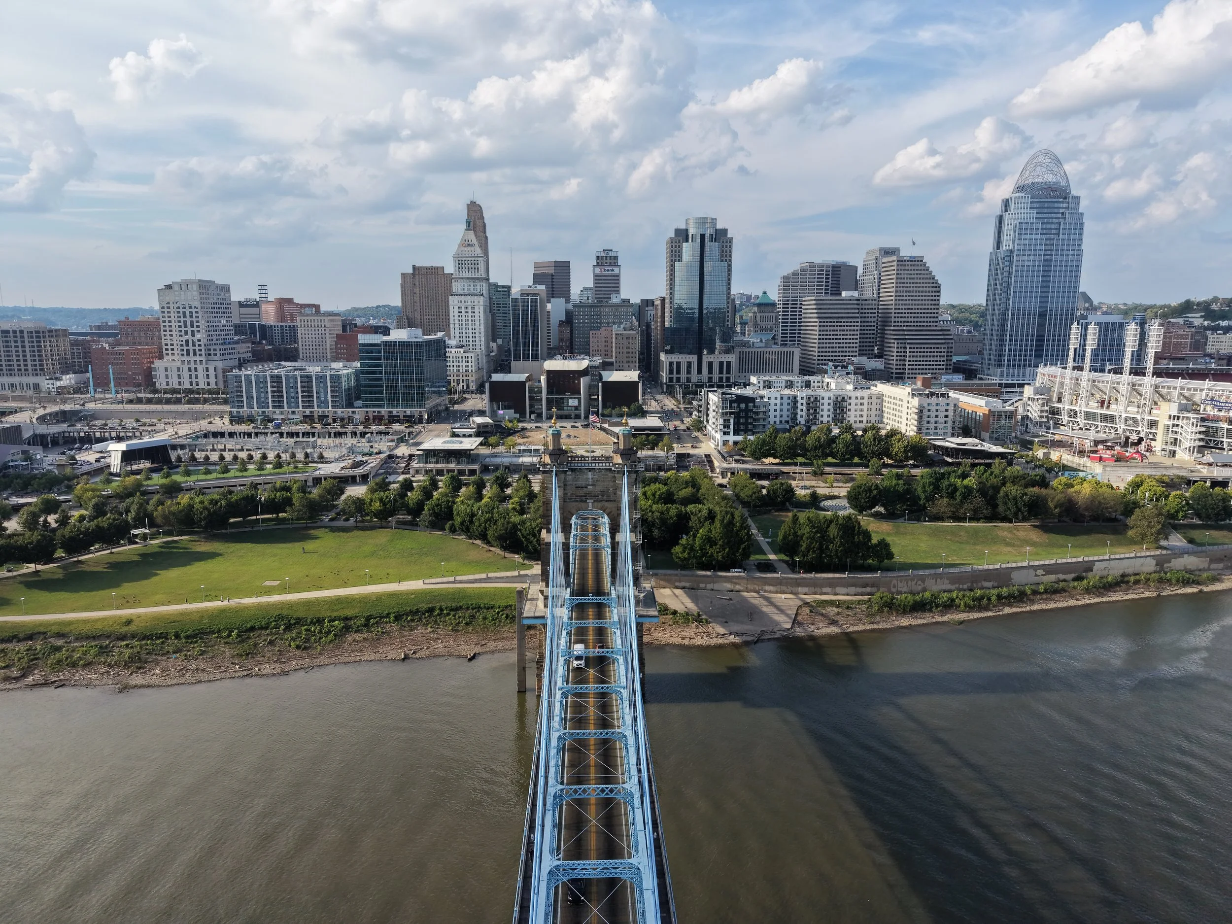 Cincinnati skyline aerial drone photo with tall buildings, including the Key Tower, and a river in the foreground. A bridge crosses over the river.