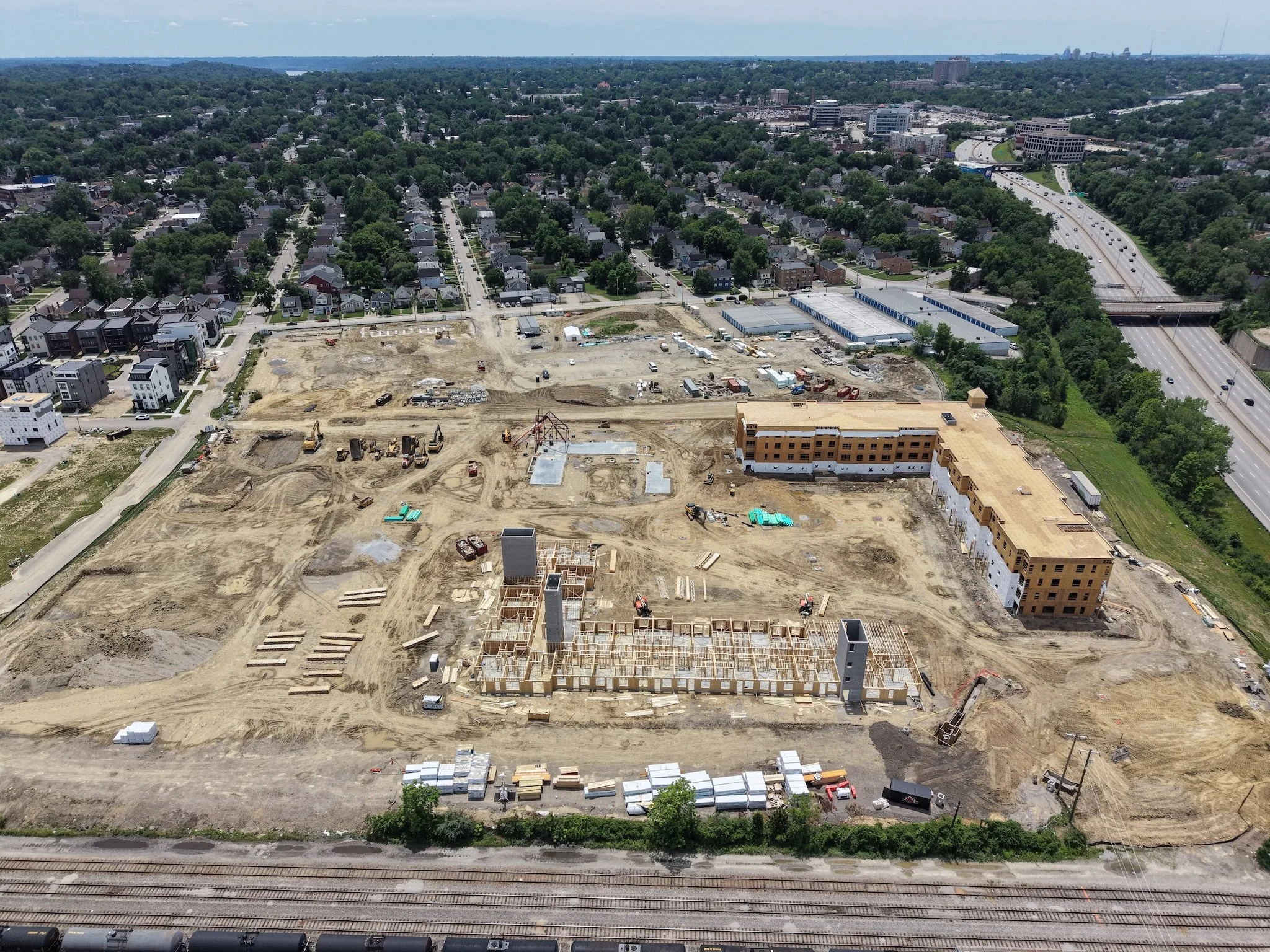 An aerial view of a construction site in a city, with buildings, roads, and a highway with traffic.