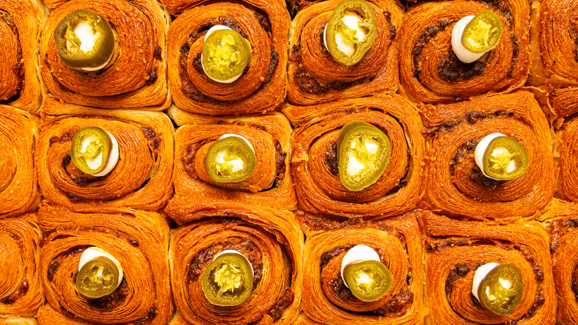 Close-up of multiple jalapeno poppers with spicy filling, topped with slices of jalapenos, arranged closely together.