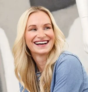 A woman with long blonde hair smiling and looking to the side.