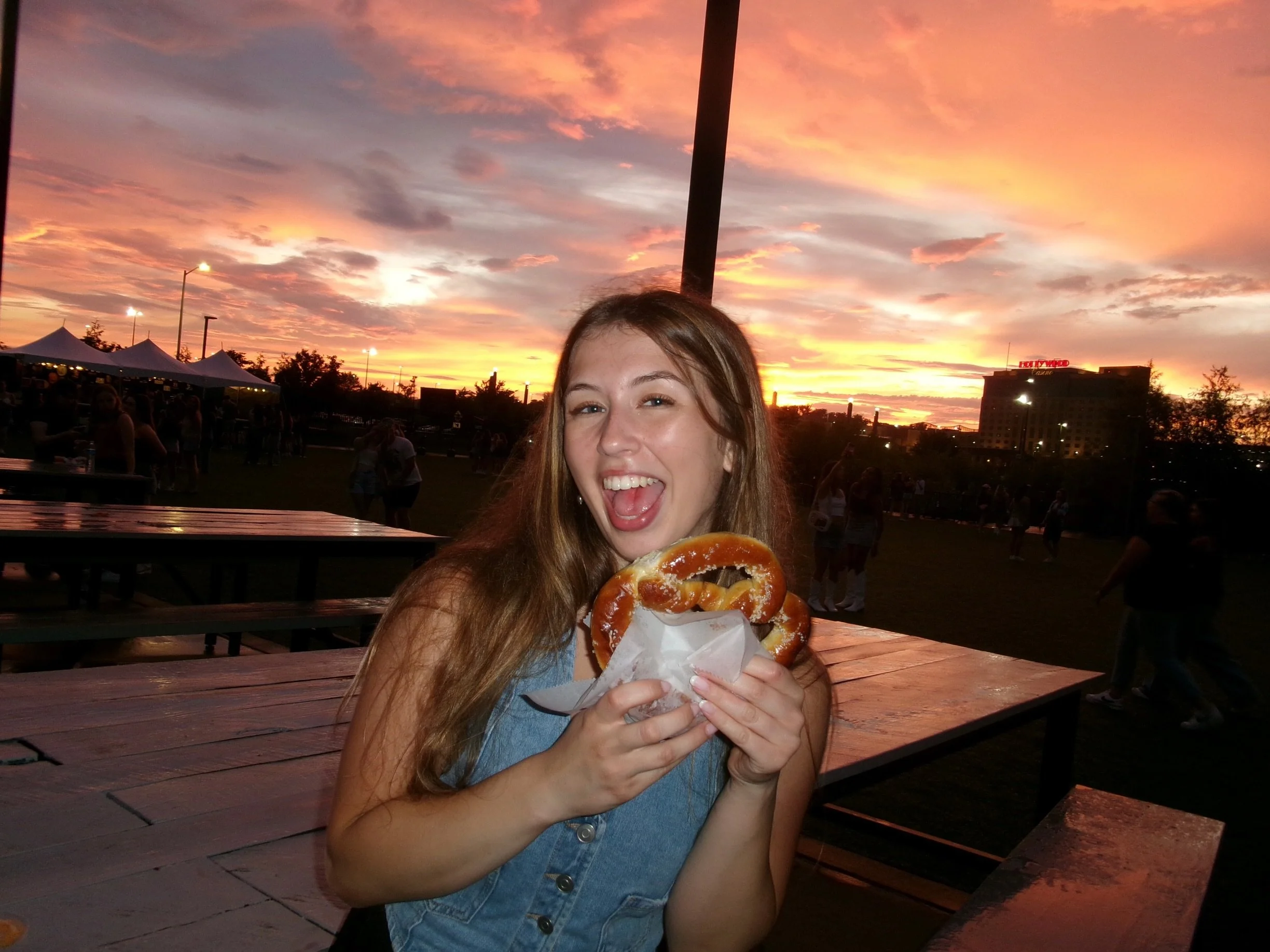 photo of Maddy, stylist, holding a giant pretzel in front of an orange sunset