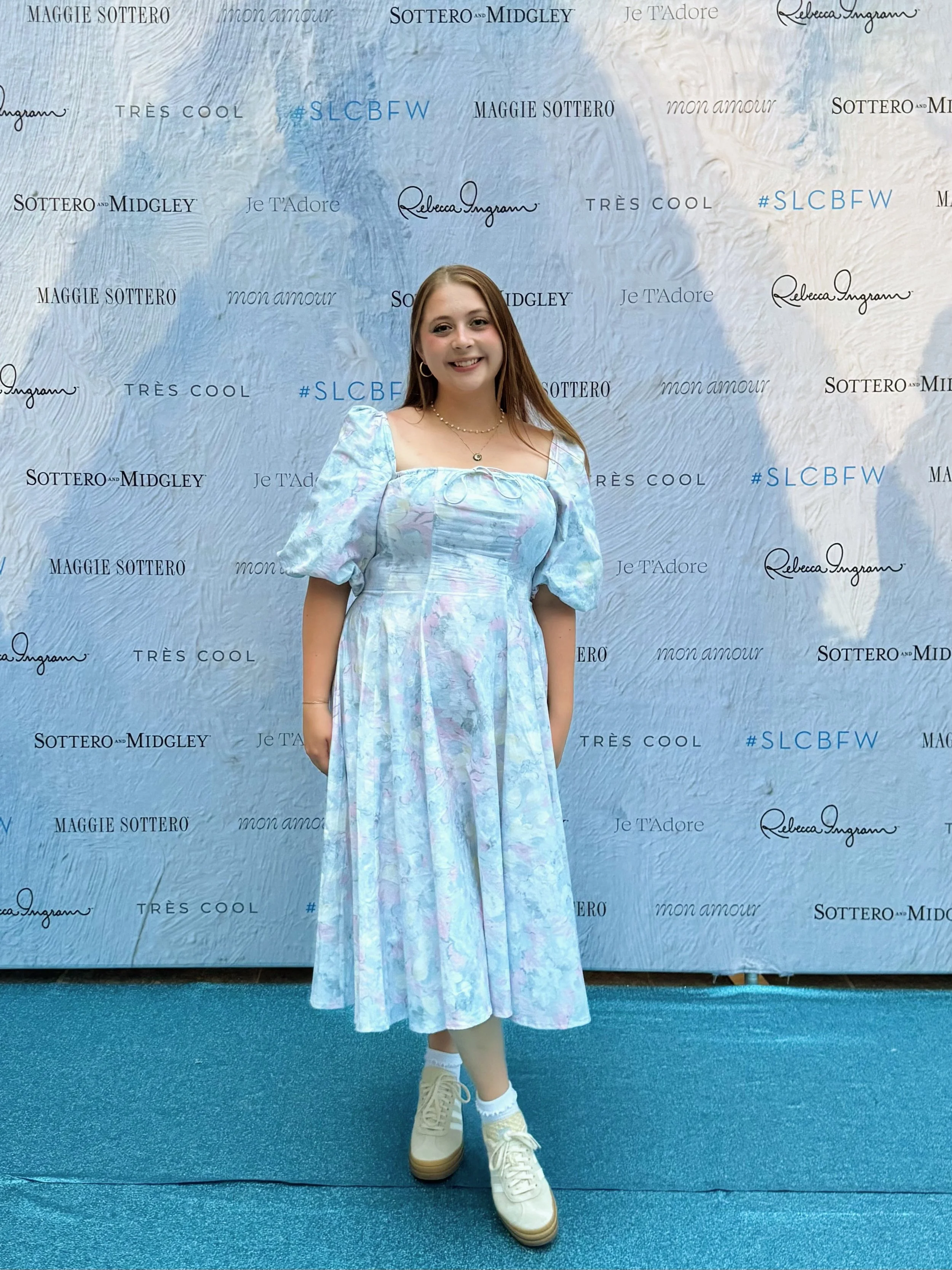 photo of Jazmyn, assistant manager, in front of a backdrop in a blue and pink dress
