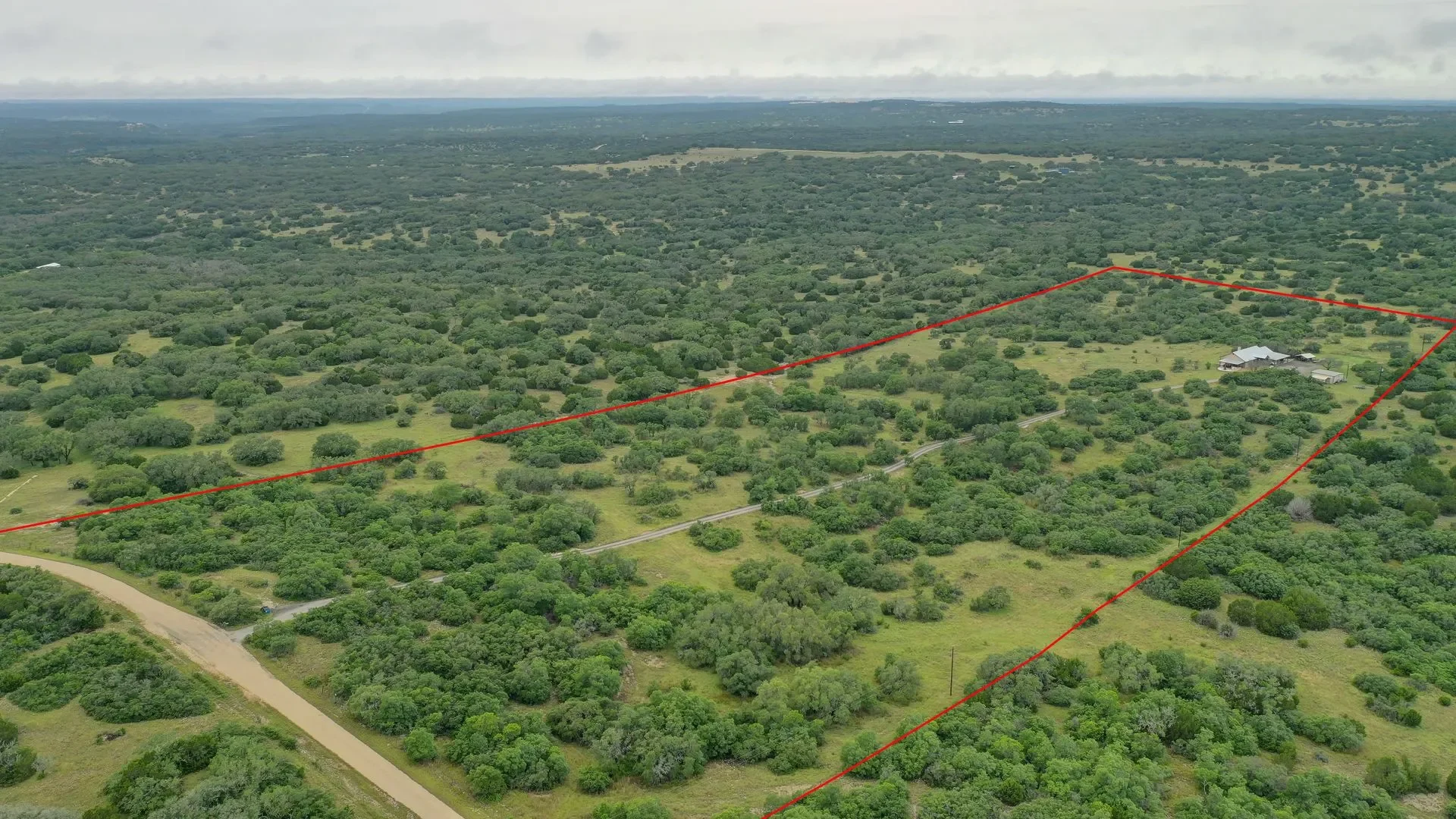 Aerial view of a large, lush green property with trees, open land, and a house, outlined by red lines indicating property boundaries.