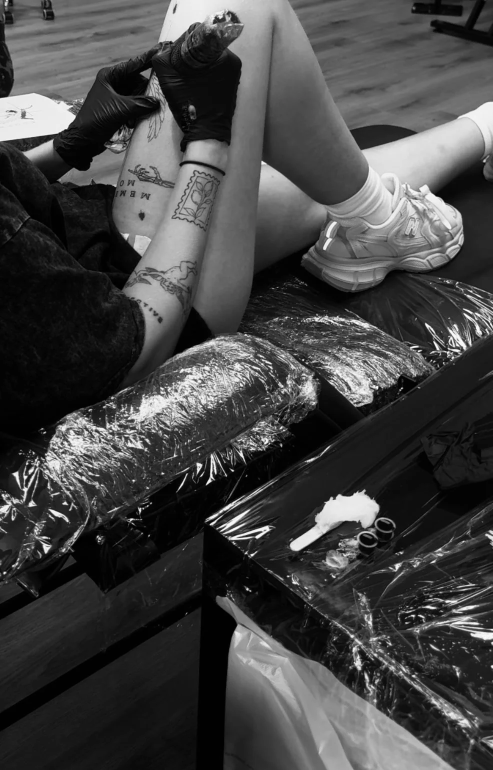 Someone getting a tattoo on their calf at a tattoo studio, with tattoo equipment and supplies on a table covered with plastic.