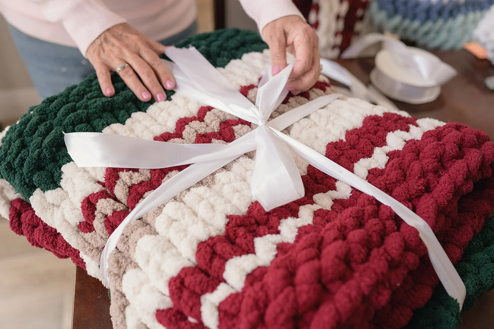 Tiani wrapping a handmade chunky knit blanket with ribbon.