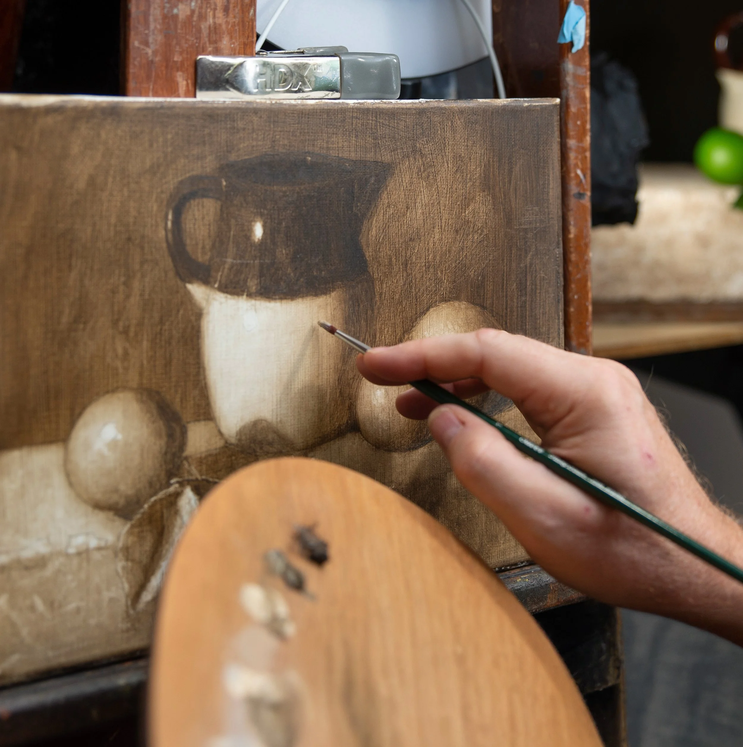 Joe Mattus painting a classical still life of a pitcher and fruit.