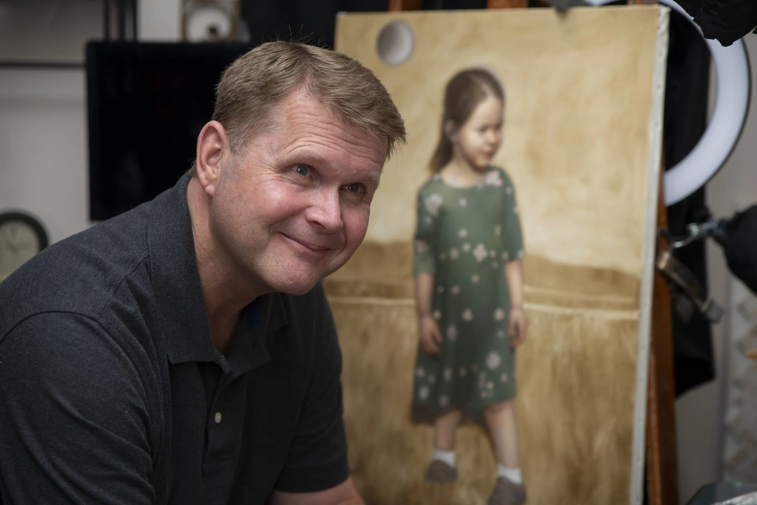 Joe Mattus in his studio beside a realistic portrait painting.