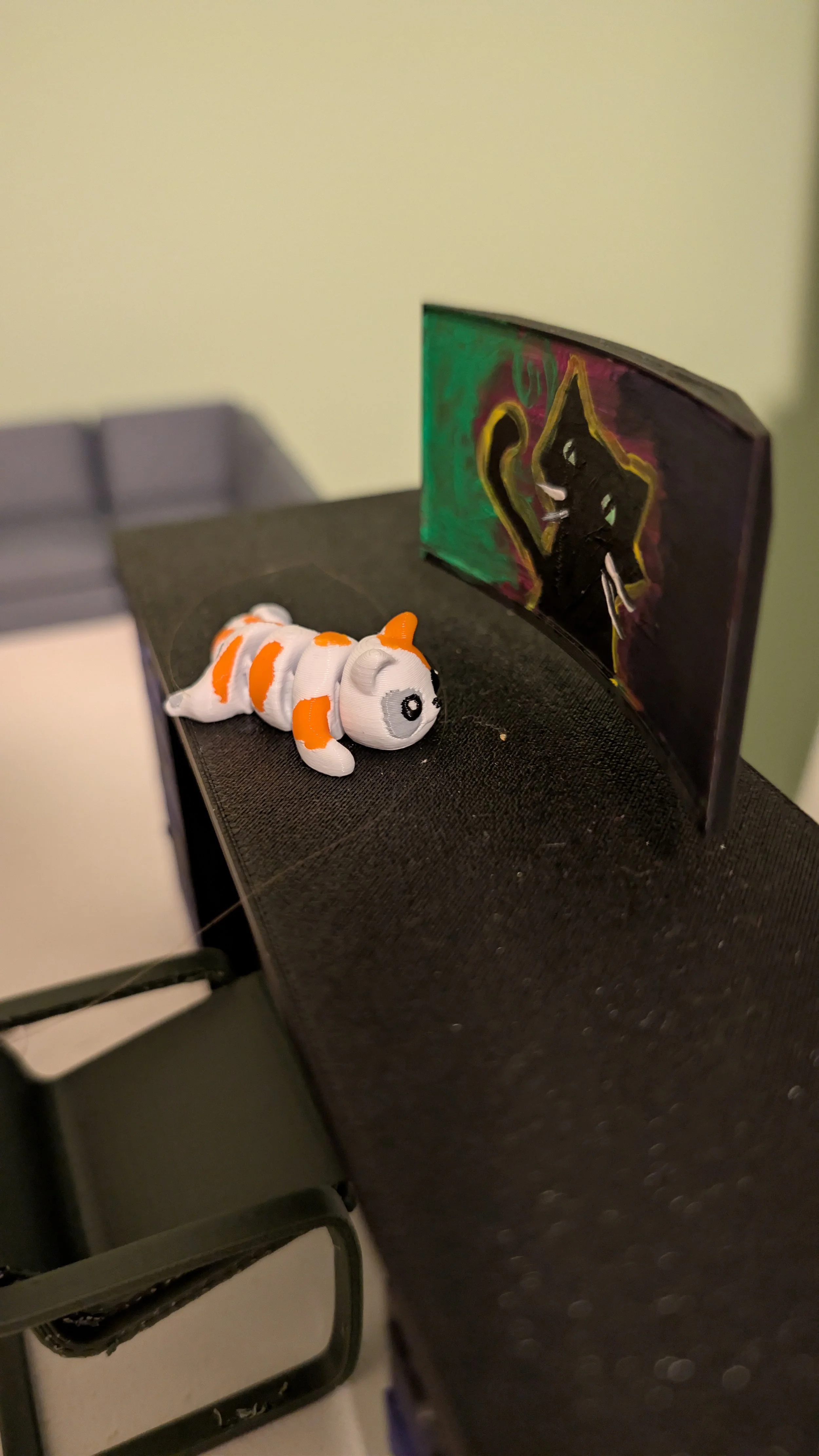 Small toy dog with white, orange and black colors lying on a black table near a colorful painting in the background.