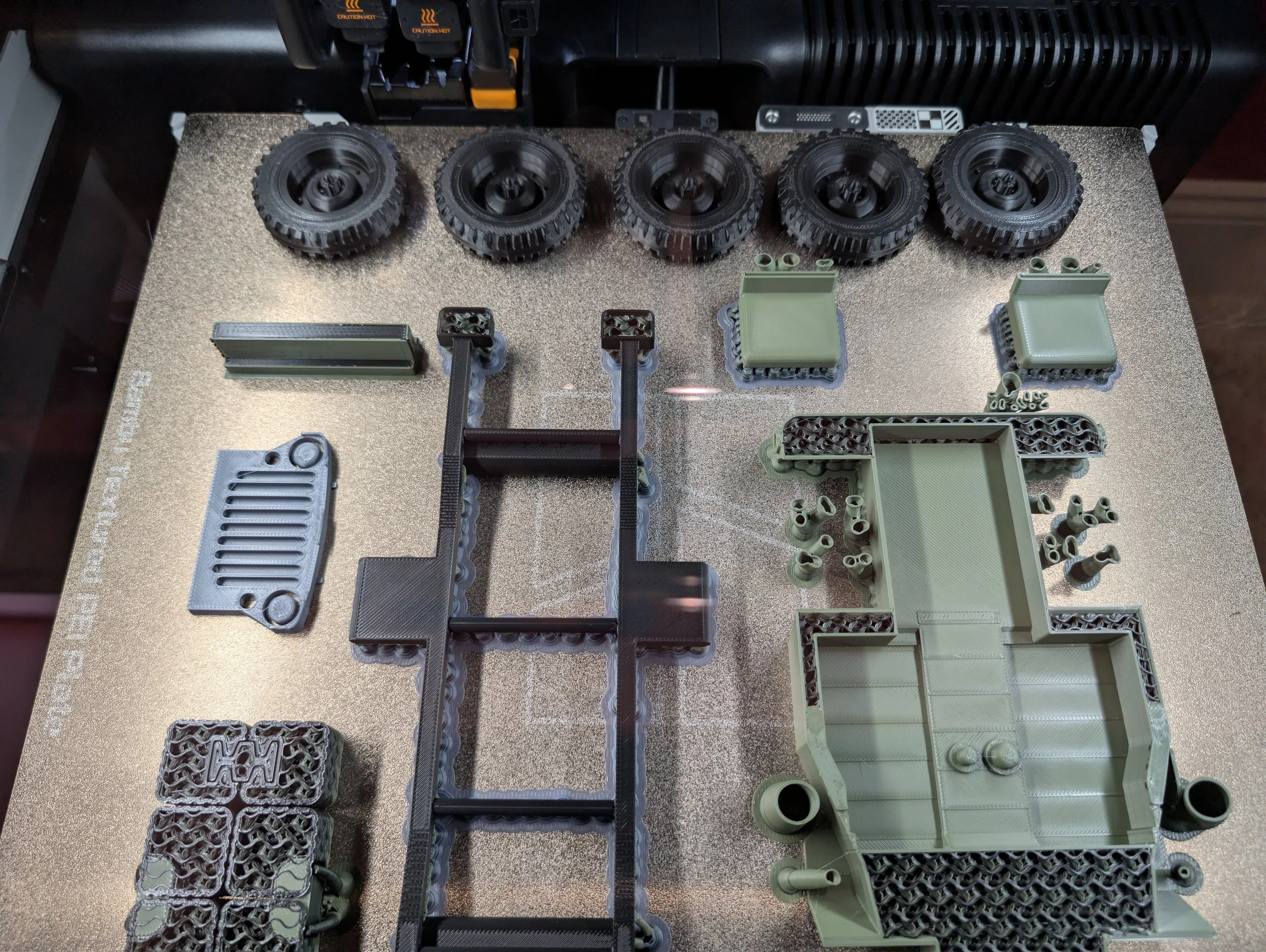 Various 3D-printed plastic parts and wheels arranged on a textured surface, with some black tires and green structural components.
