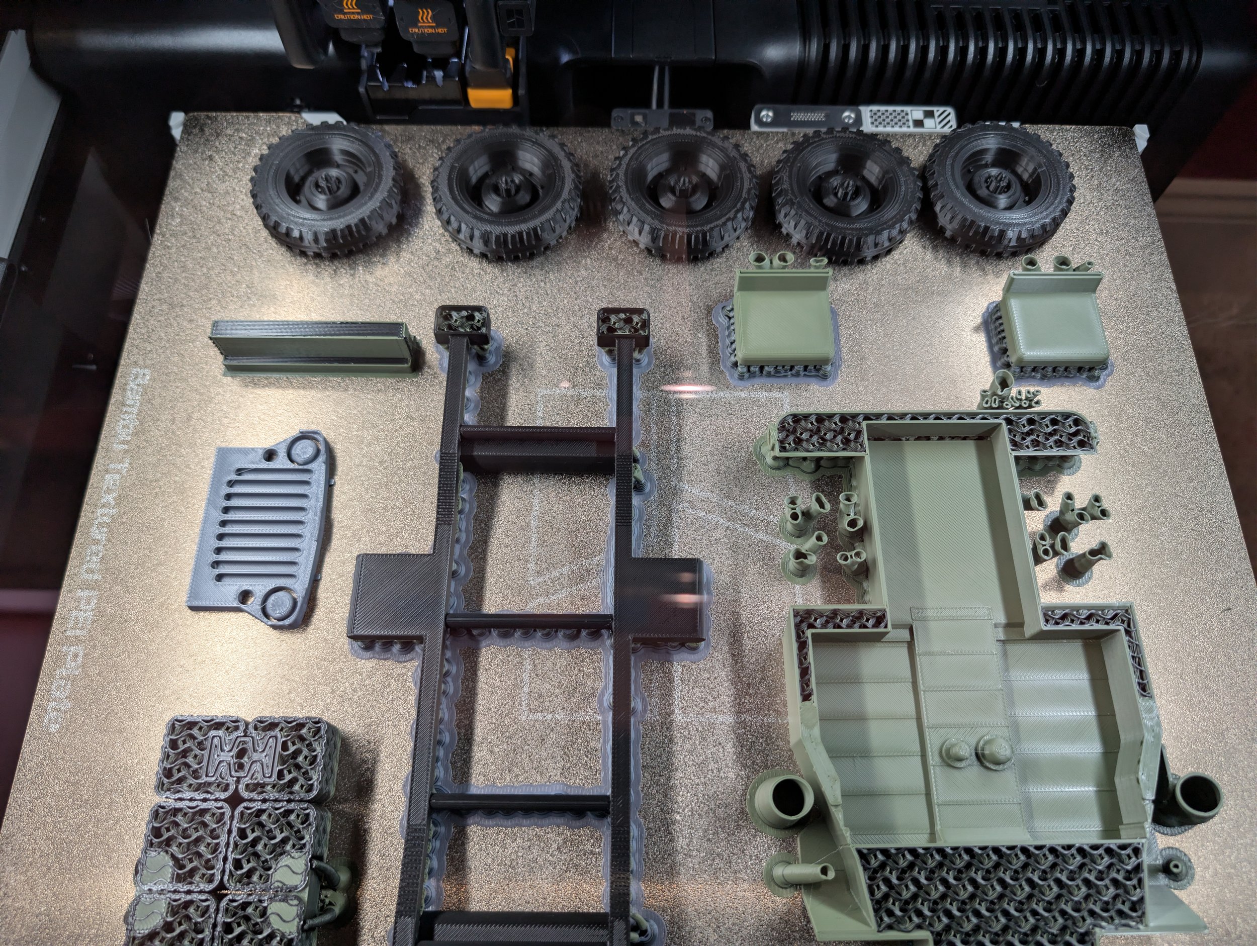 Various 3D-printed plastic parts and wheels arranged on a textured surface, with some black tires and green structural components.