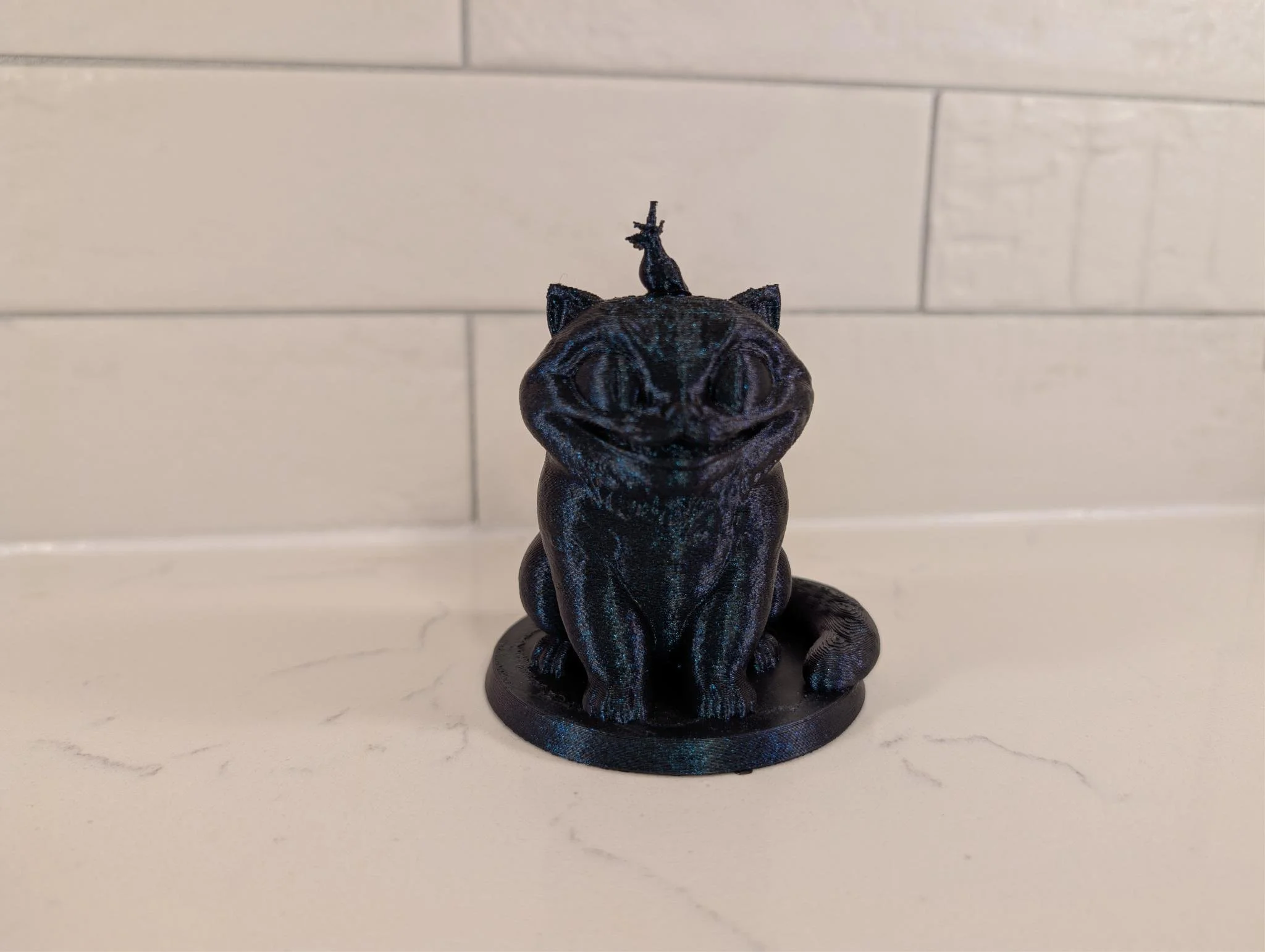 A small, black, and shiny figurine of a mythical creature with a unicorn horn, sitting on a round black base on a white marble surface against a beige tiled wall.
