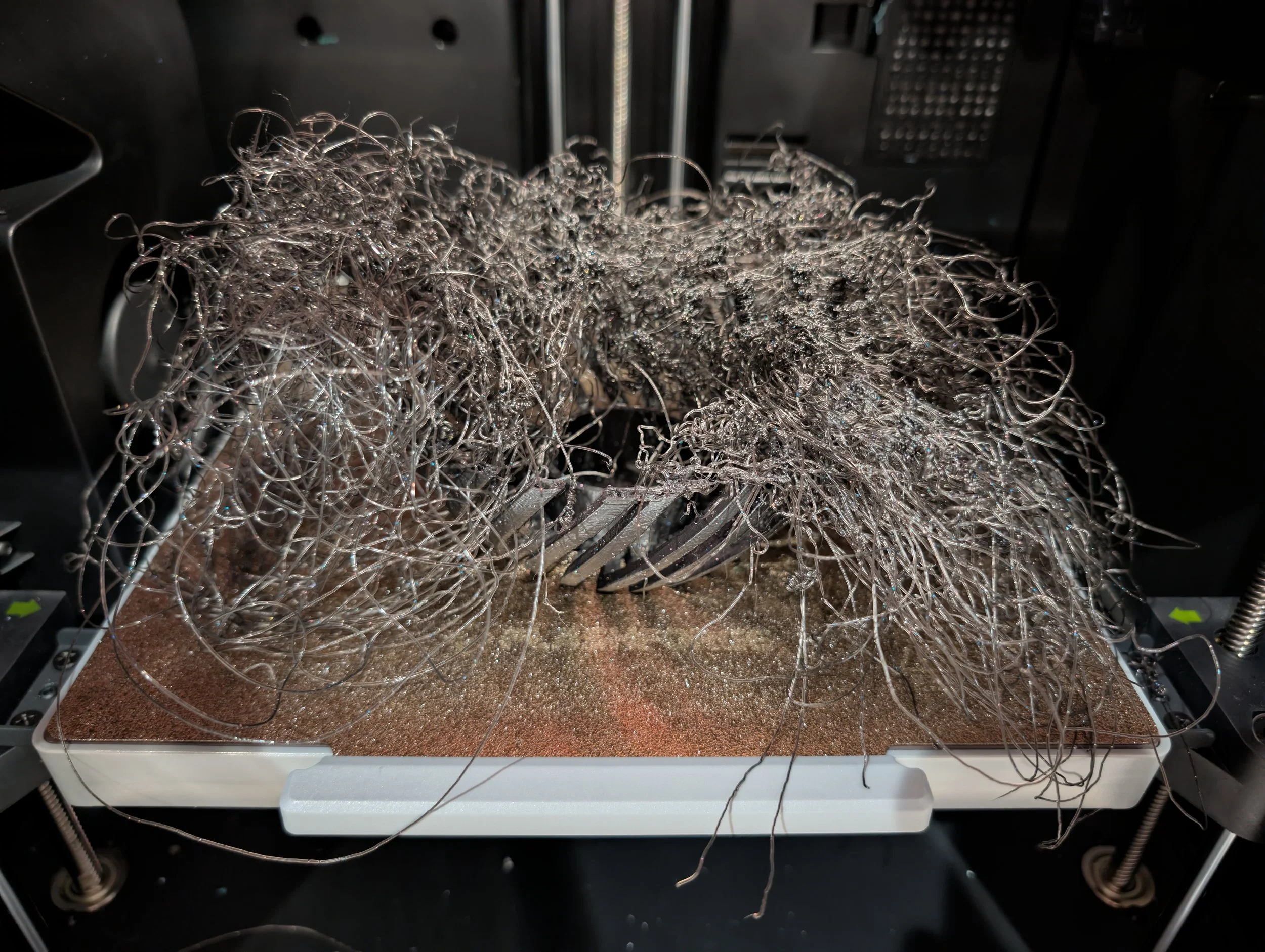 A 3D printer's heated bed with a tangled heap of metallic resin support structures printed on it.