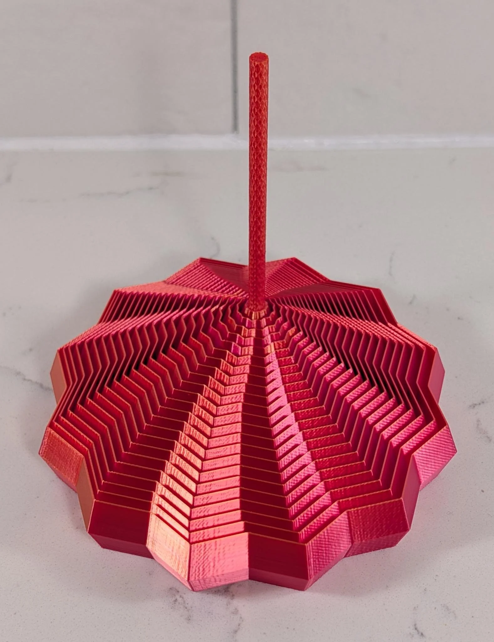 A red origami paper umbrella with a hexagonal shape, open and placed on a white marble surface.