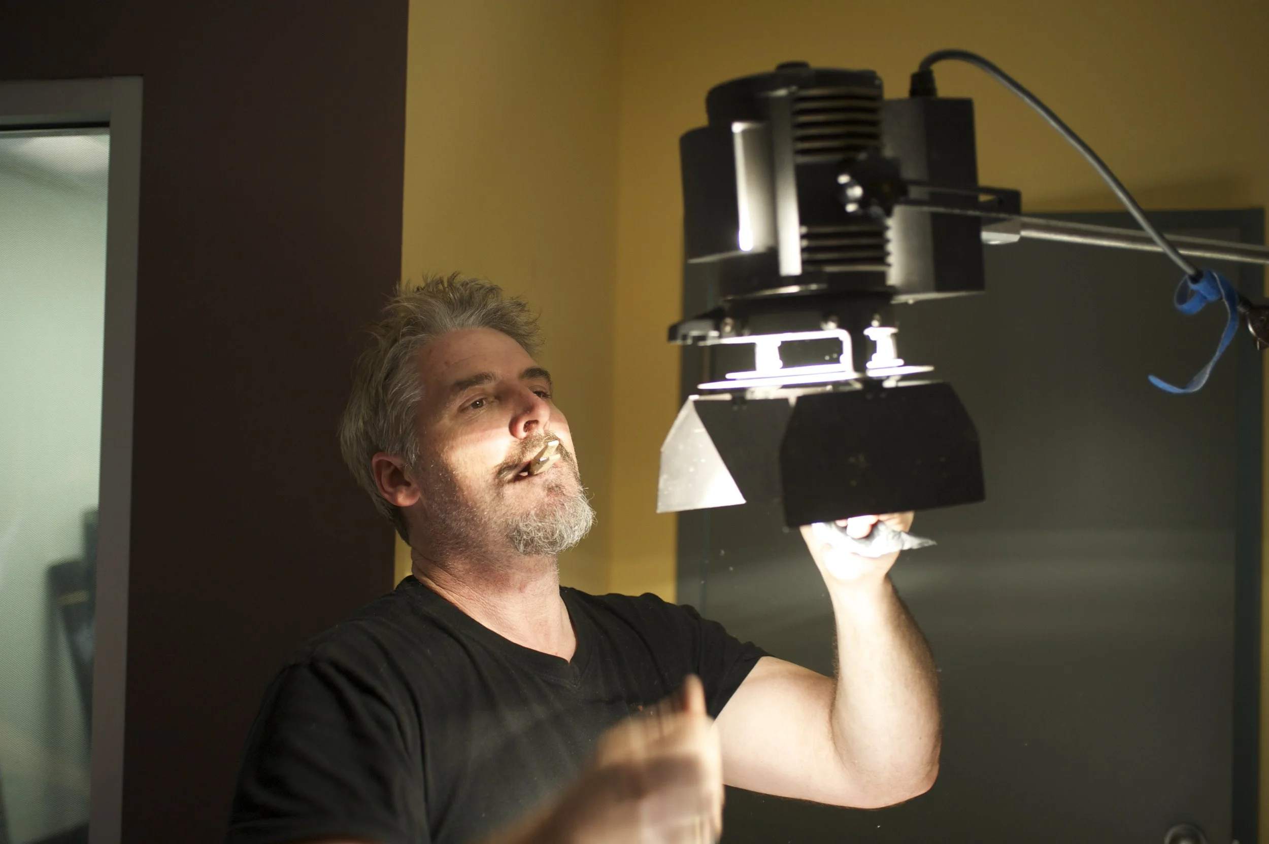 Man in a black shirt adjusting a large studio light fixture indoors
