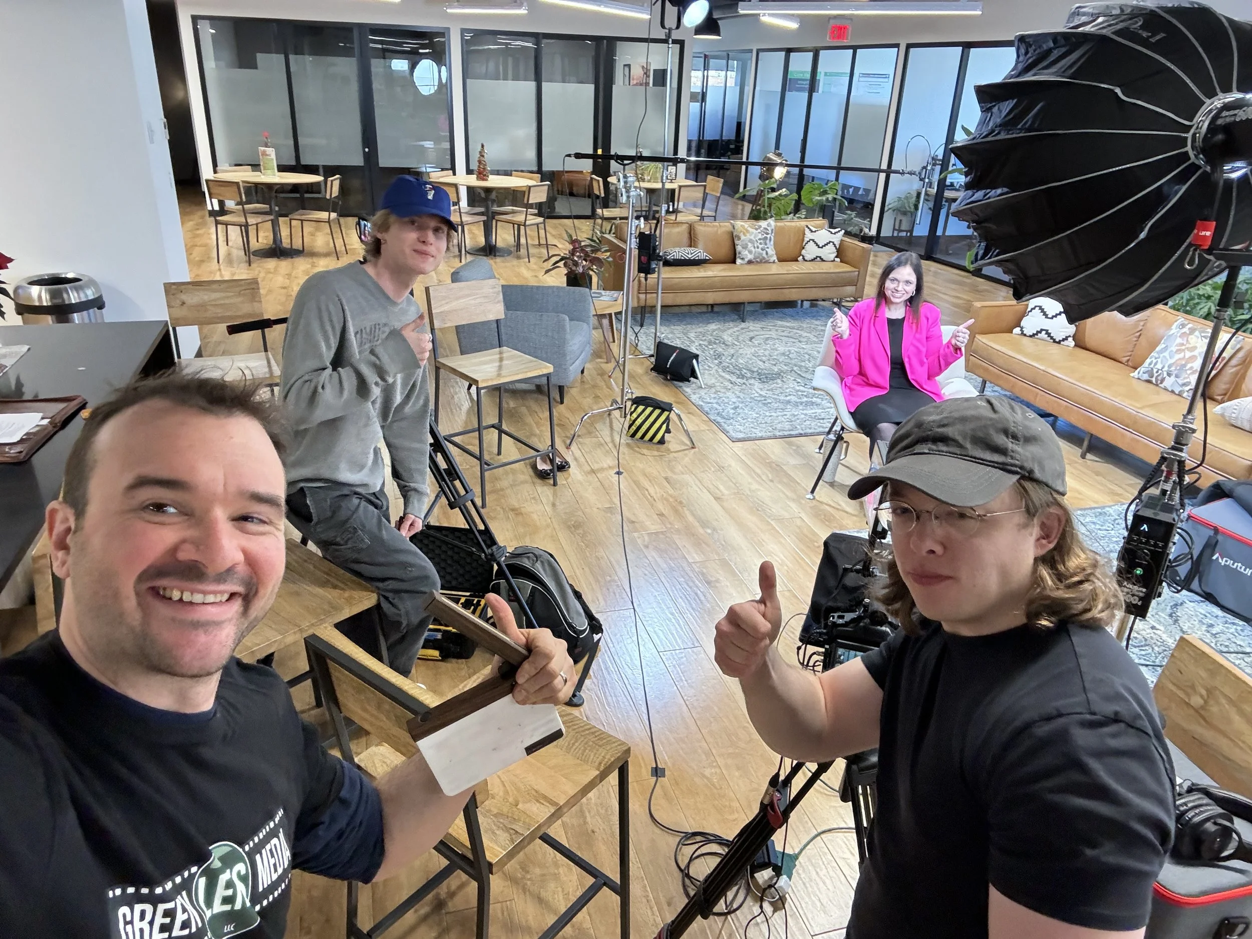 Film crew posing in a modern cafe studio with cameras, lighting equipment, couches, and tables.