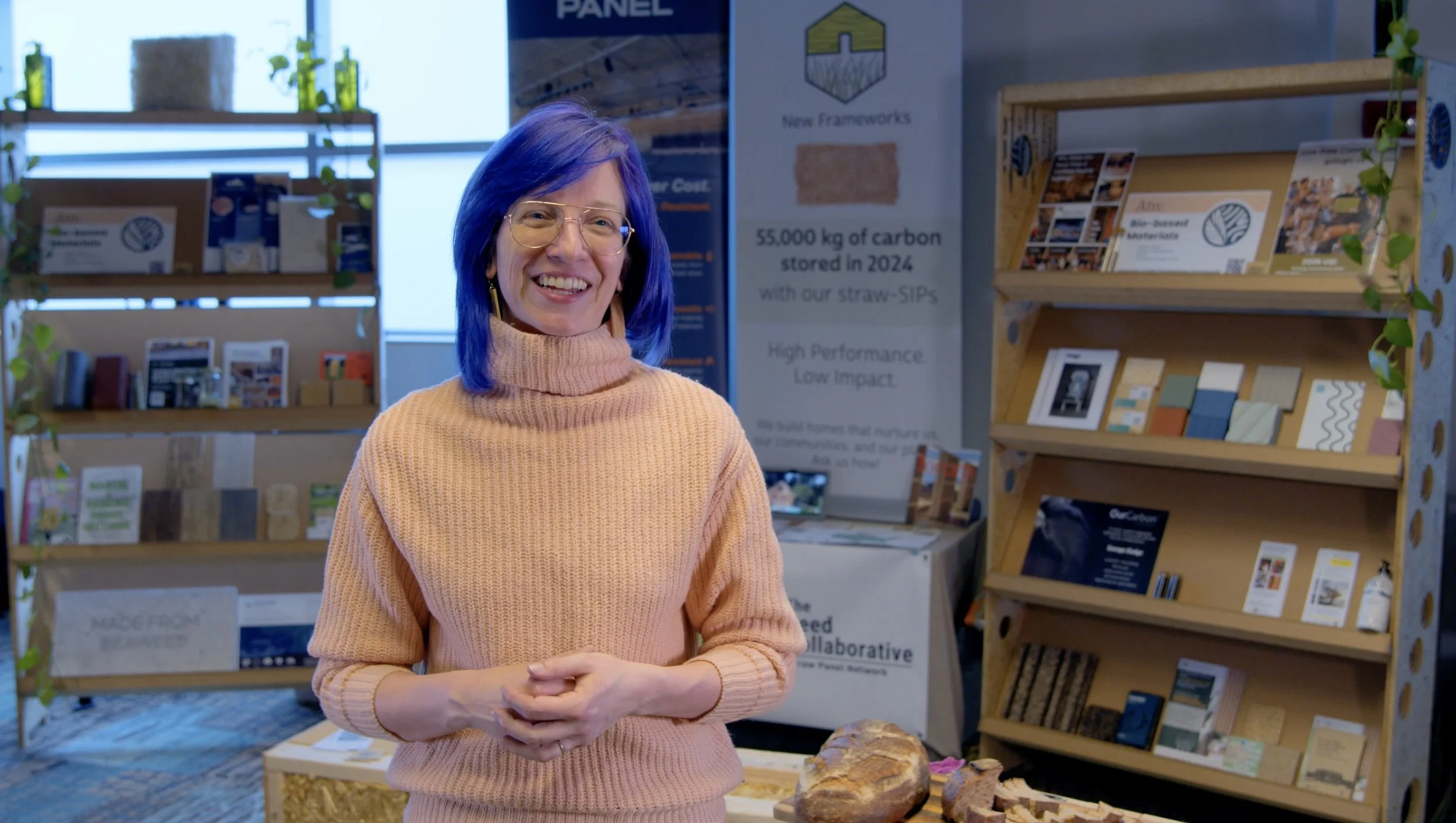 Smiling woman with blue hair and glasses standing in a sustainable building materials showroom.