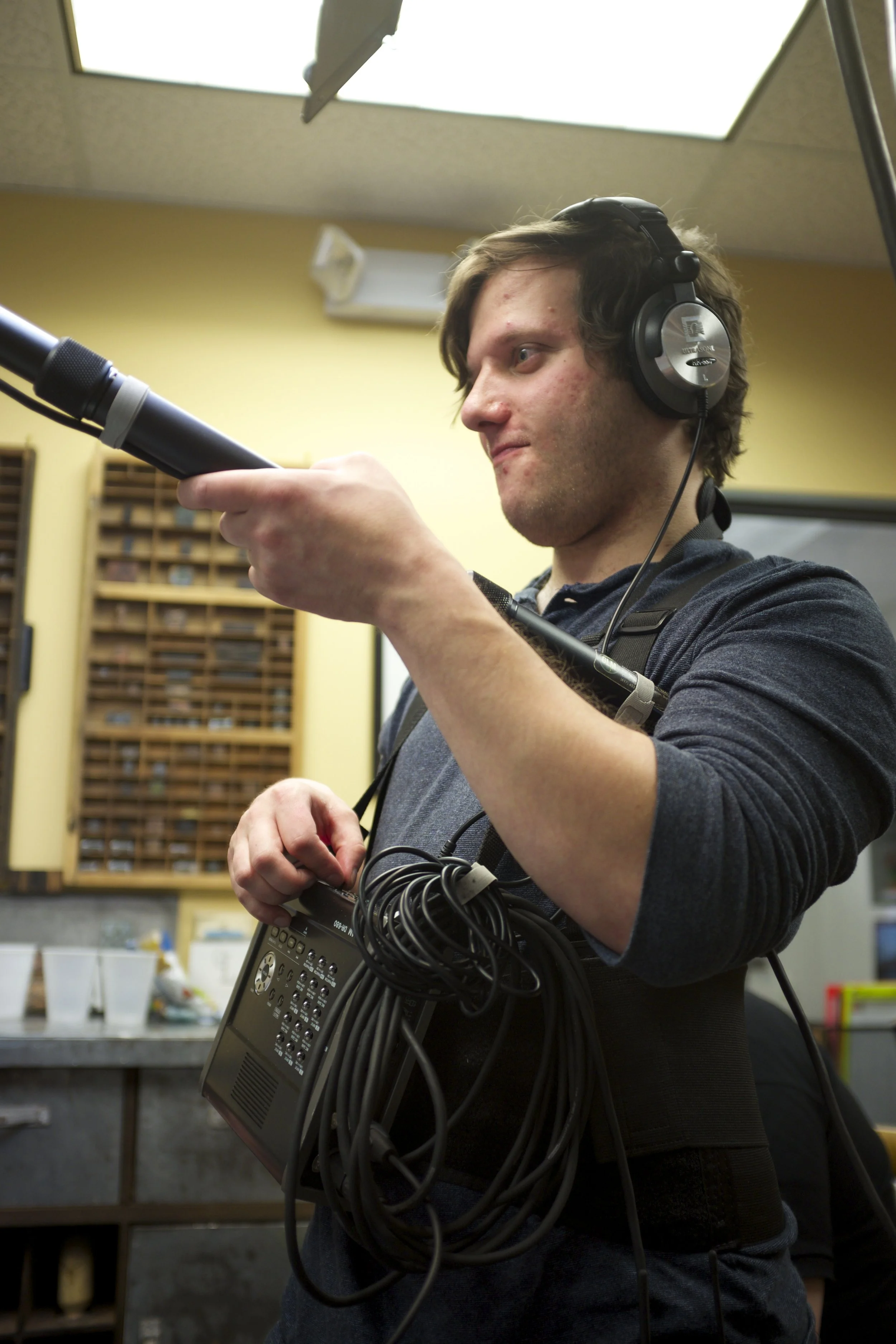 Sound technician wearing headphones and holding a boom microphone and portable audio mixer indoors