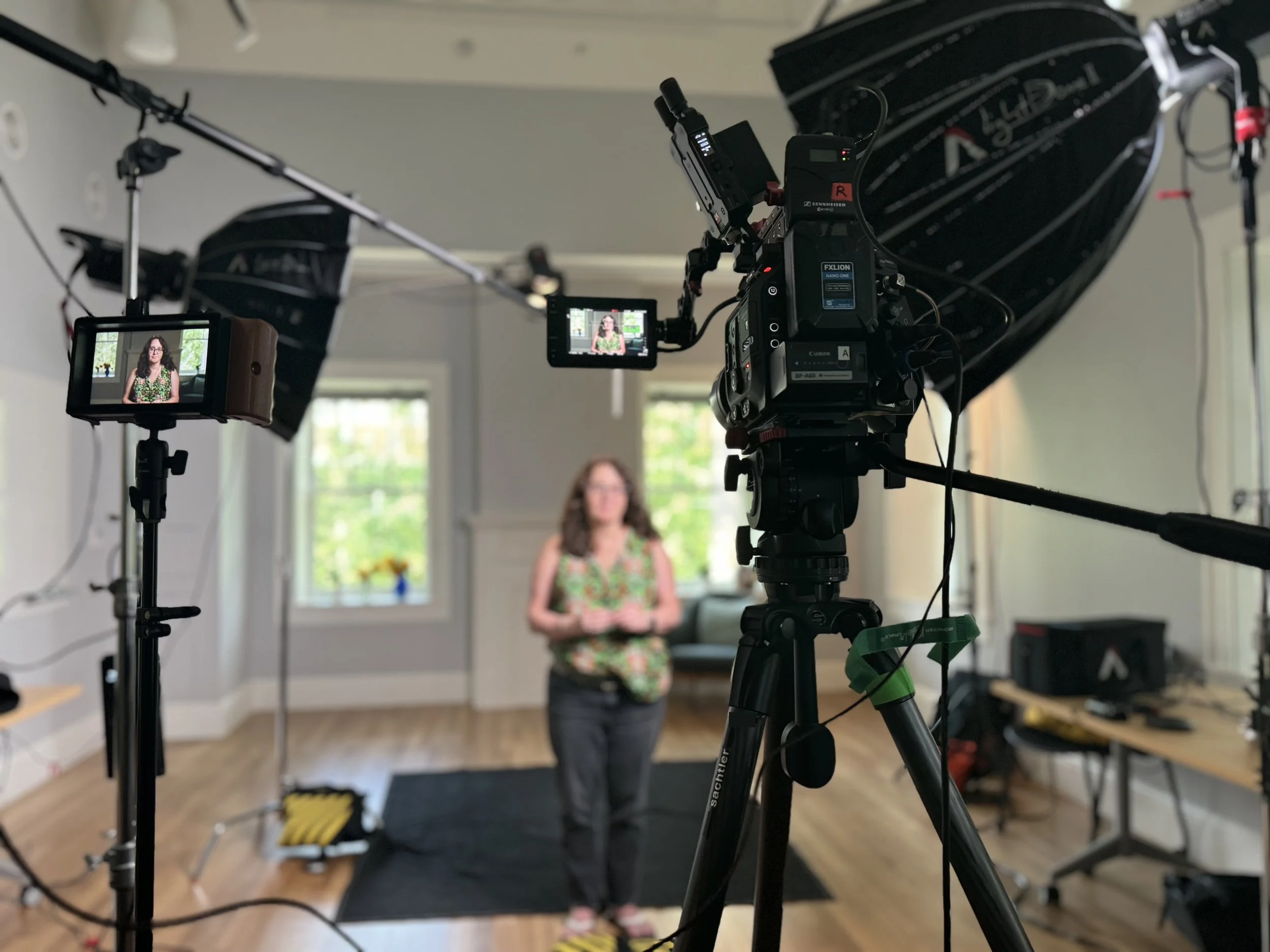 Indoor video production setup with cameras, studio lights, and a woman in a floral top being recorded.