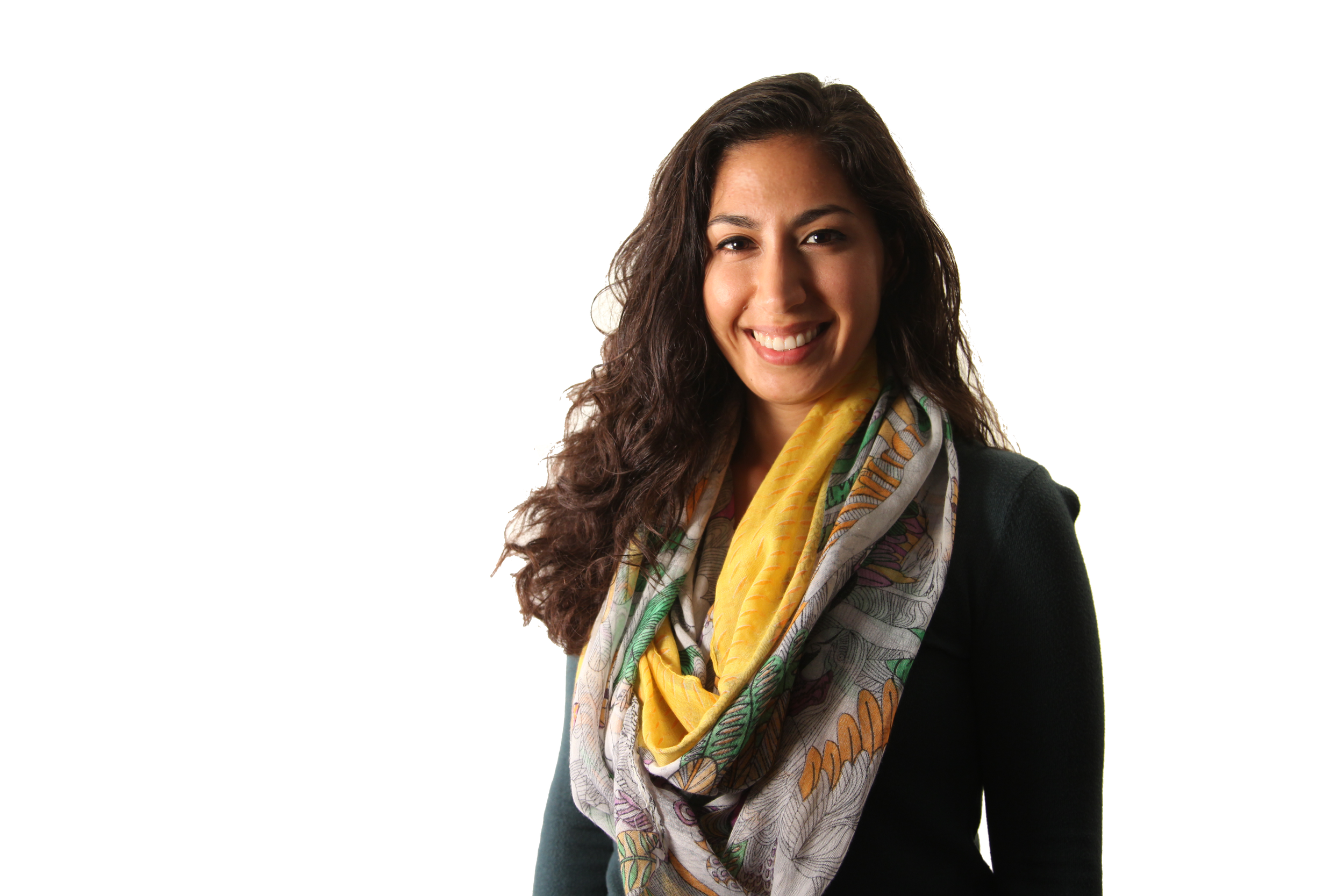 Smiling woman with long dark hair wearing a colorful patterned scarf and black blazer against a white background