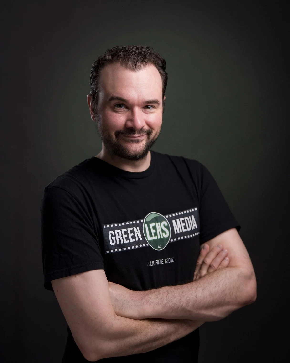 Portrait of a smiling bearded man with folded arms wearing a Green Lens Media T-shirt