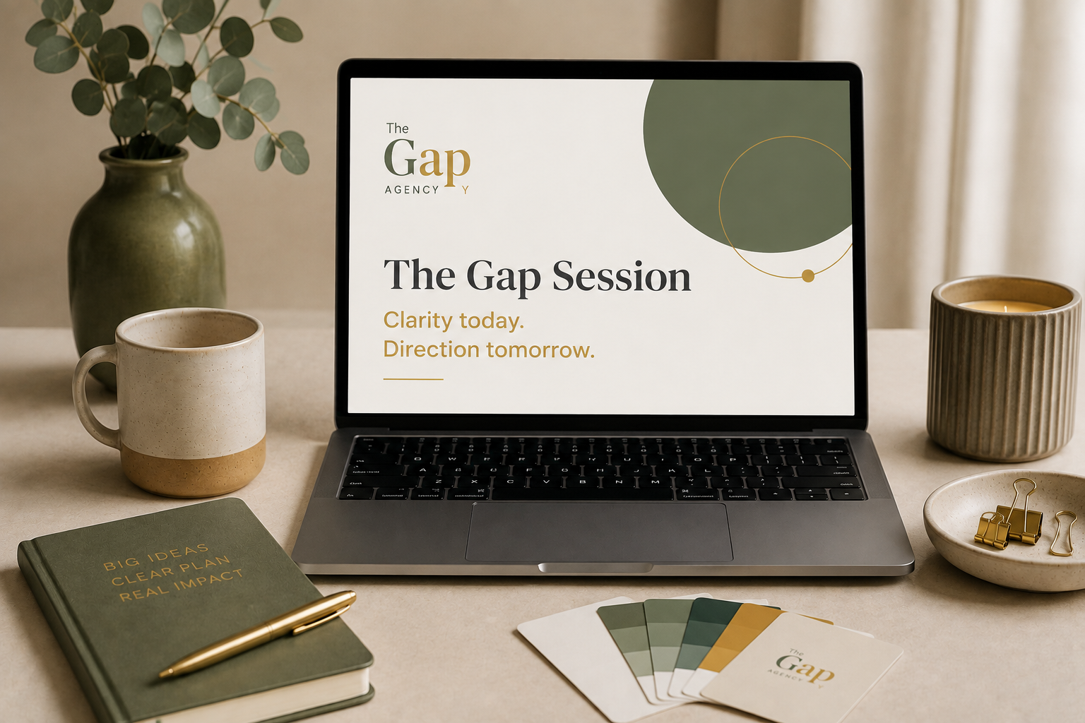 A laptop displaying a presentation titled 'The Gap Session' with the subtitle 'Clarity today. Direction tomorrow.' A green potted plant, a coffee mug, a tray with gold clips, a closed notebook with 'Big Ideas, Clear Plan, Real Impact' written on it, a gold pen, and color swatches are arranged on a desk with cream-colored surface and curtains in the background.