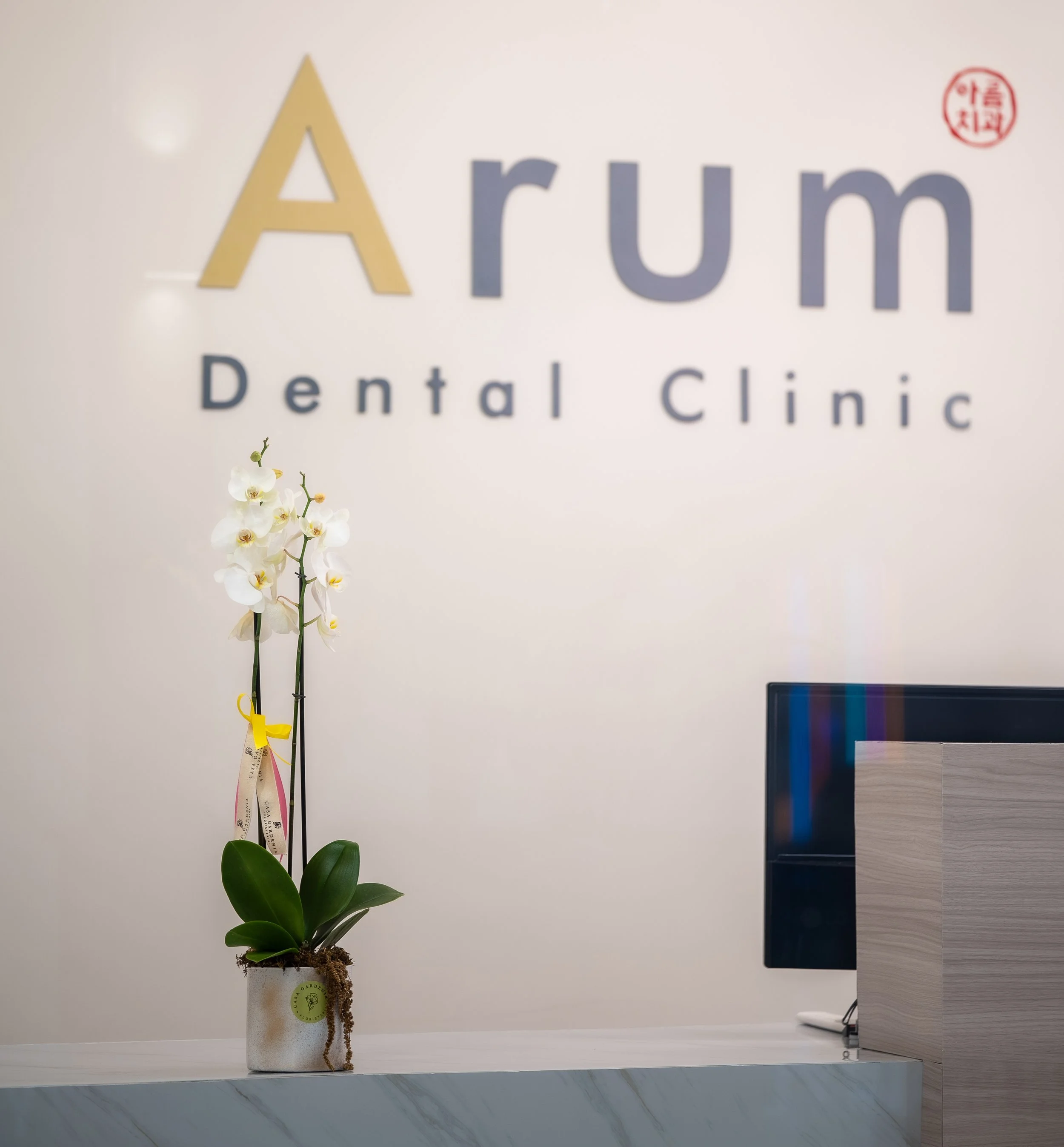 하얀 벽에 'Arum Dental Clinic'라는 간판이 붙어 있고, 앞에 하얀색 화분에 목련이 꽂혀 있음.