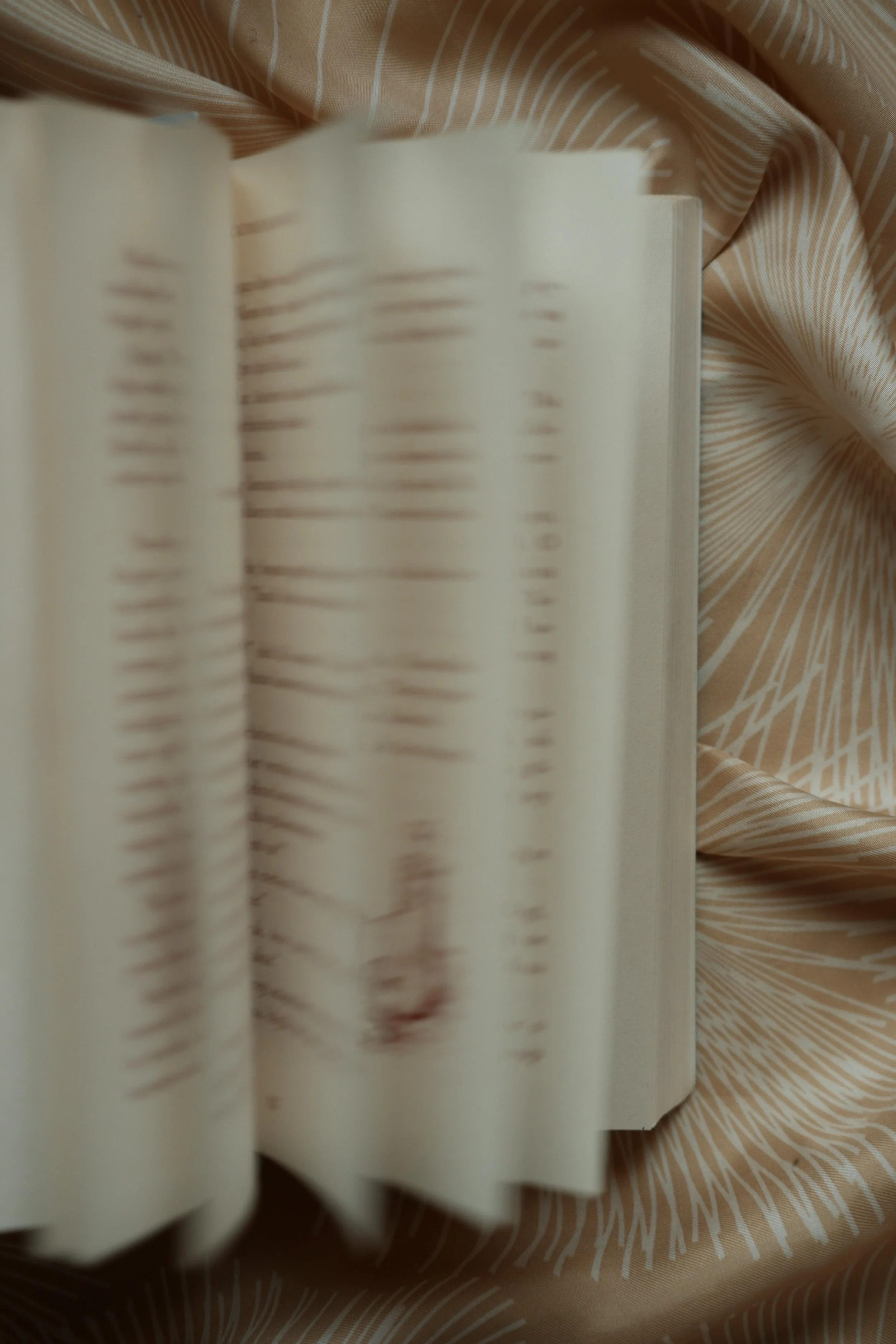 An open book with blurred text, resting on a fabric with a beige and white pattern.