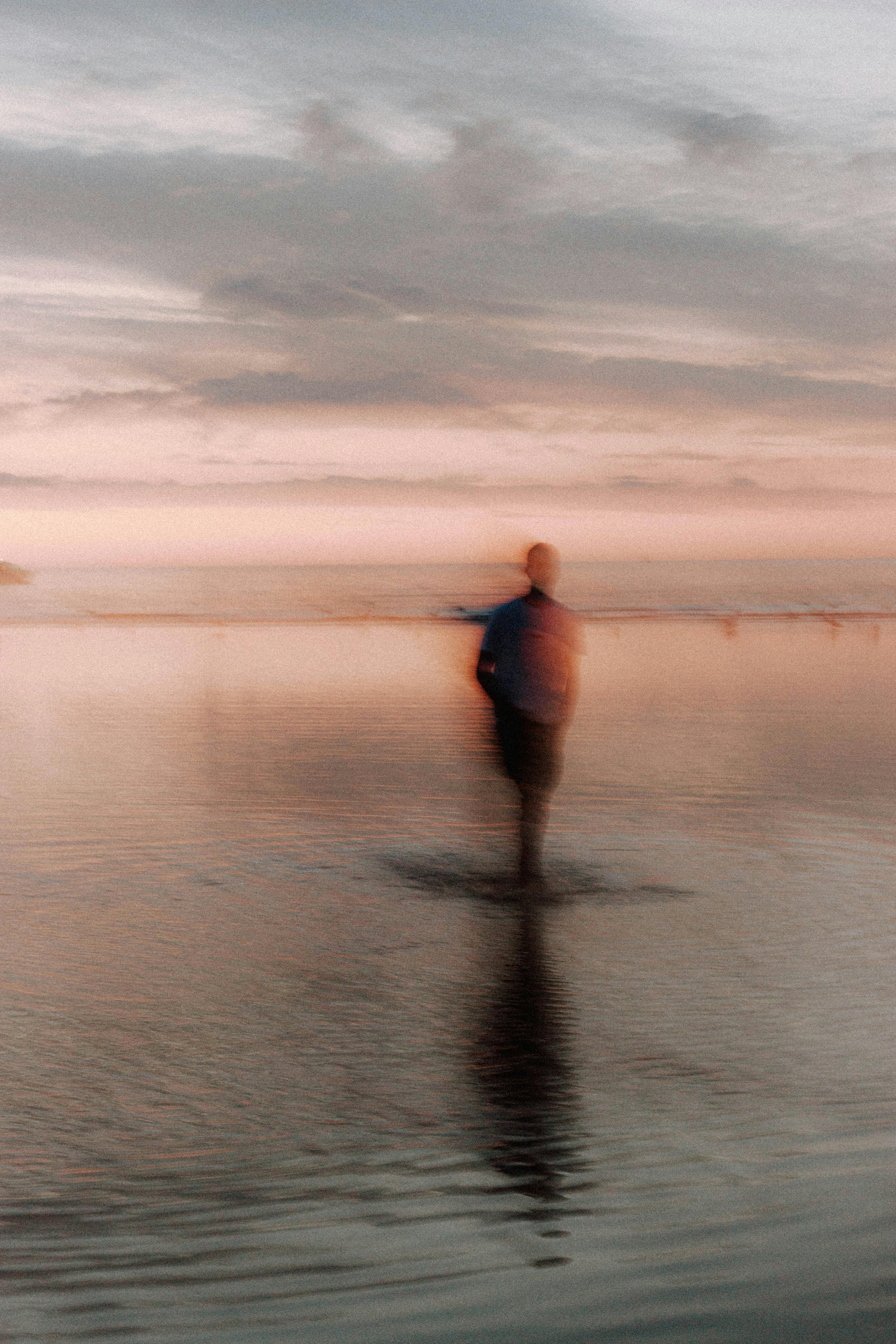 A person walking on a beach during sunset, with clouds over the ocean in the background.