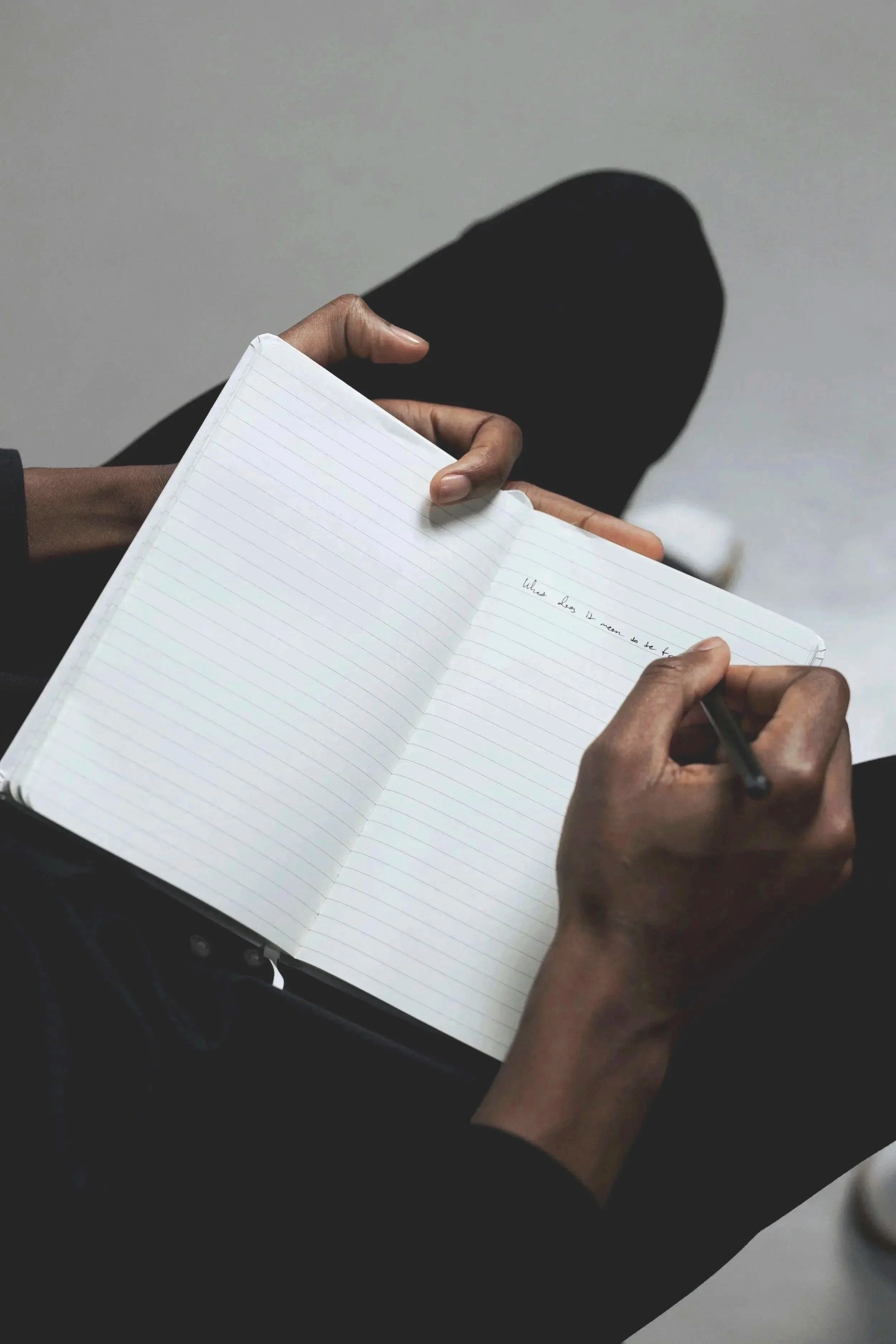 Person holding an open notebook with lined pages, writing with a pen, shadow of the person's head visible on the wall behind.