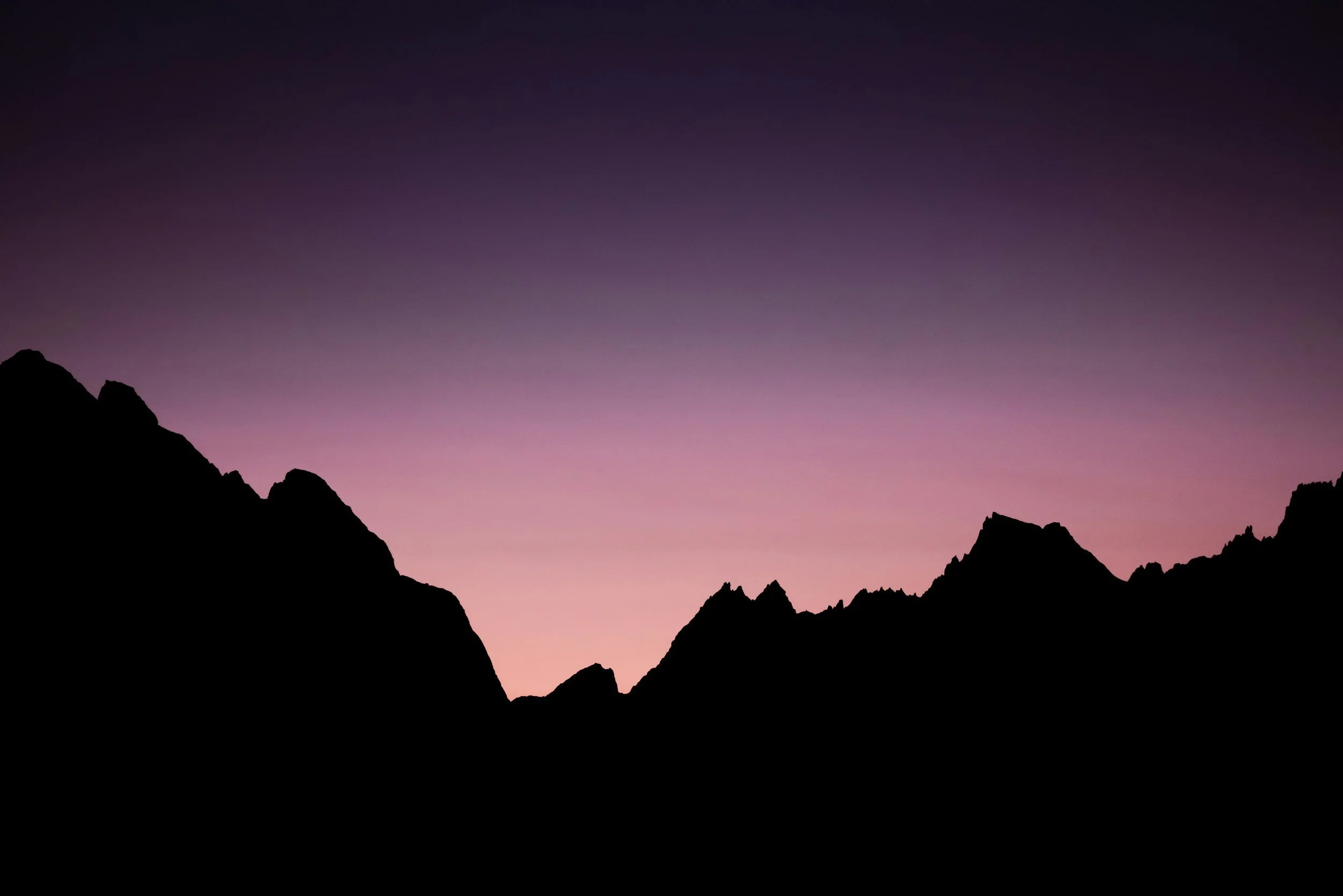 Silhouette of mountain peaks against a purple and pink twilight sky.