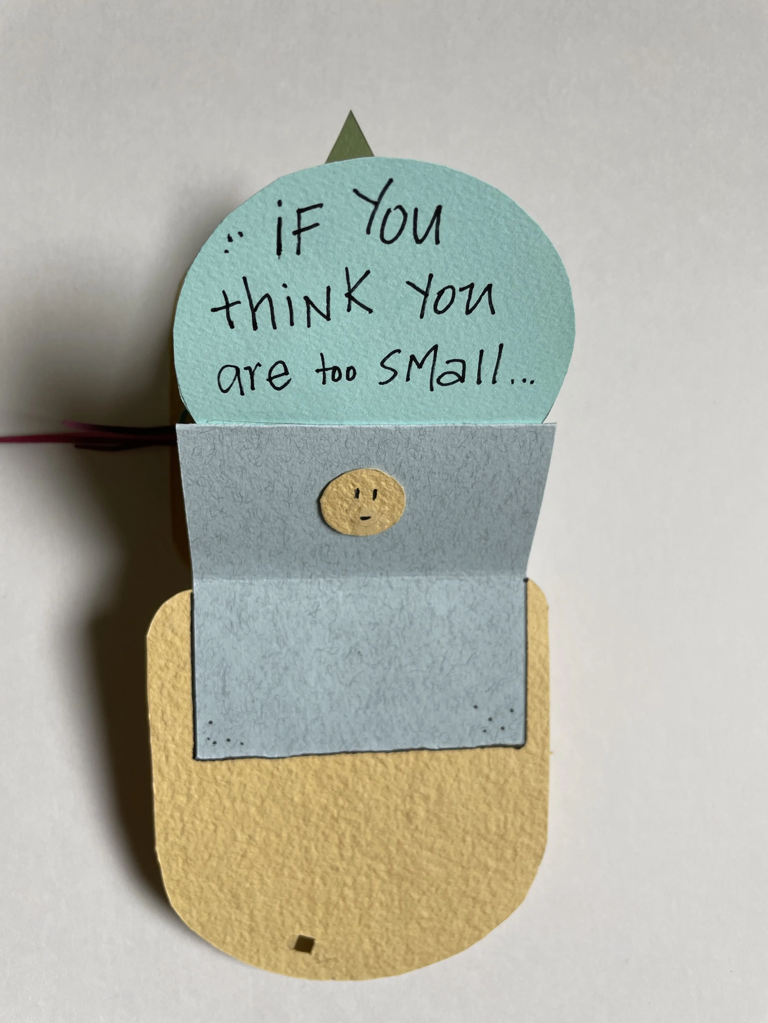 Paper craft of a flower pot with a blue circular paper saying 'If you think you are too small...' with a small smiling face on the pot, and a yellow oval paper underneath.