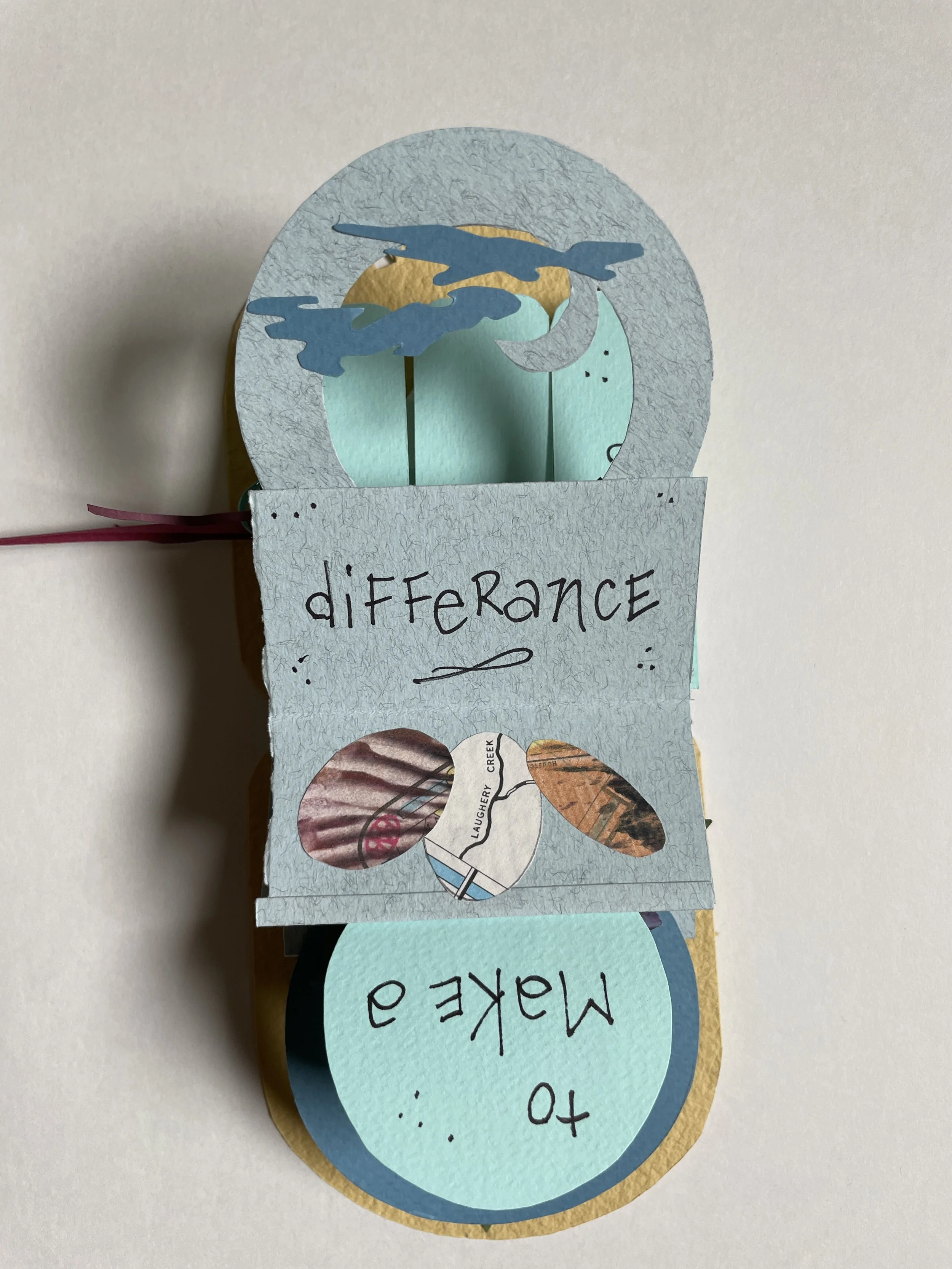 A handmade craft project with cutouts of animals and words, including a cutout of a bird and a butterfly, and words like 'to make a difference' and 'to' visible. The craft appears to be made of colored paper or cardstock, layered and decorated.