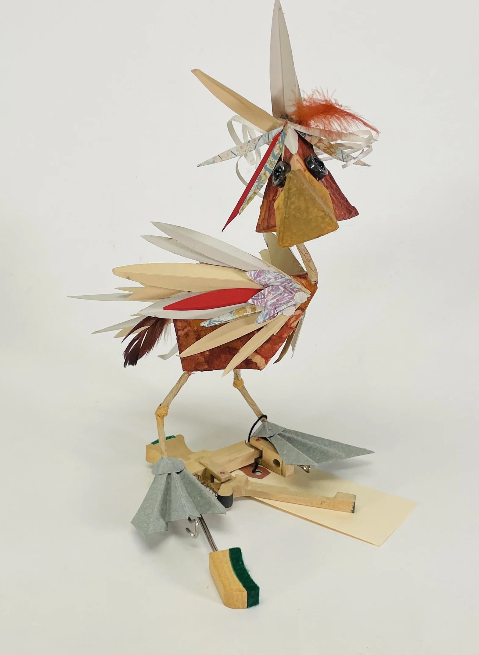 Perky red and beige paper cut bird standing on a piano key