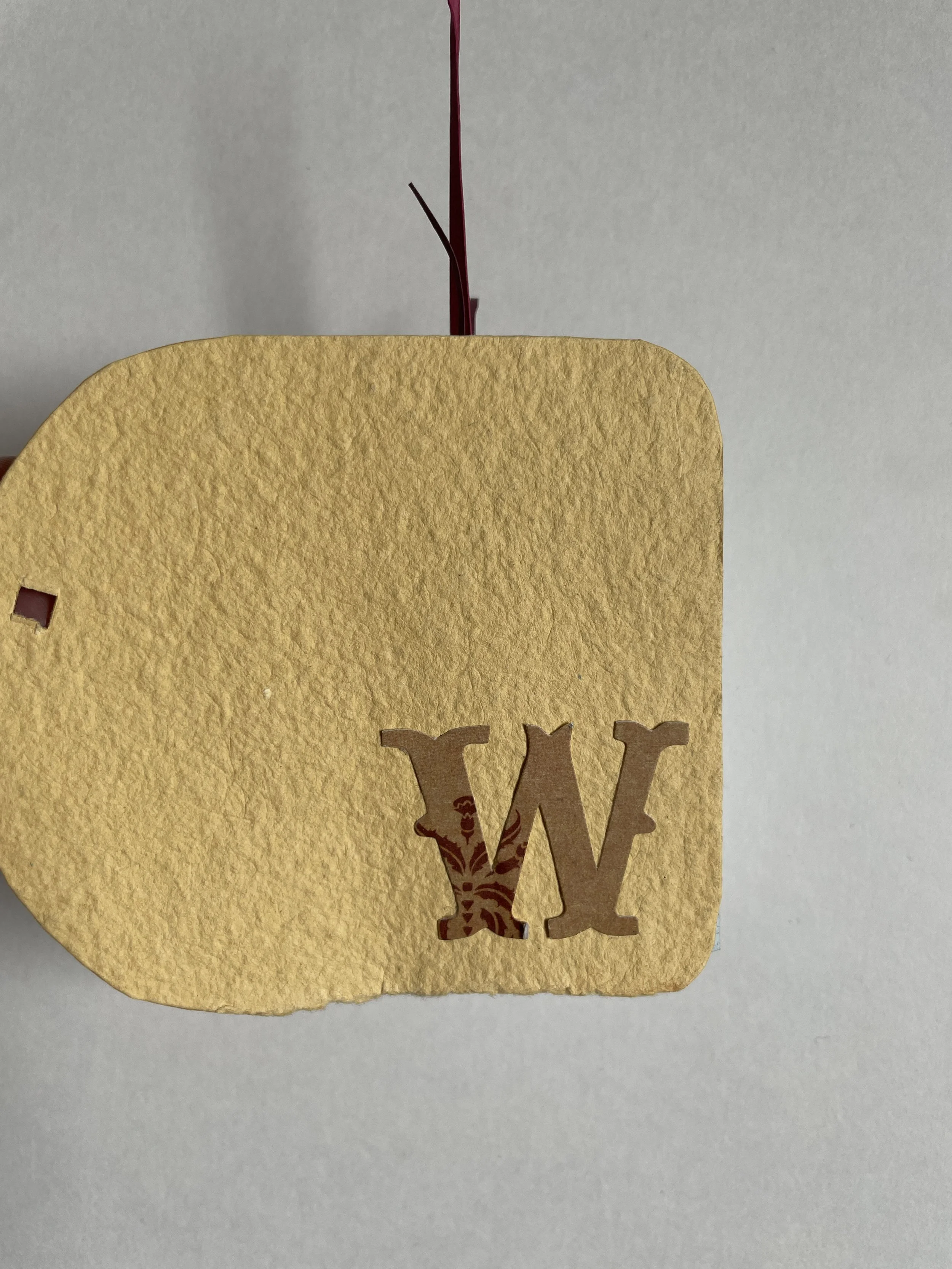 A yellow textured paper with a cutout of the letter 'W' and an intricate design, partially covered by a larger yellow paper with rounded edges, against a light gray background.