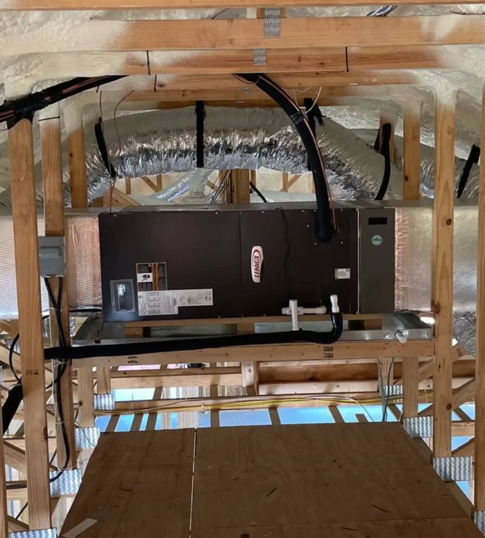 View of an HVAC furnace with ductwork and wiring installed in the ceiling framing of a building under construction.