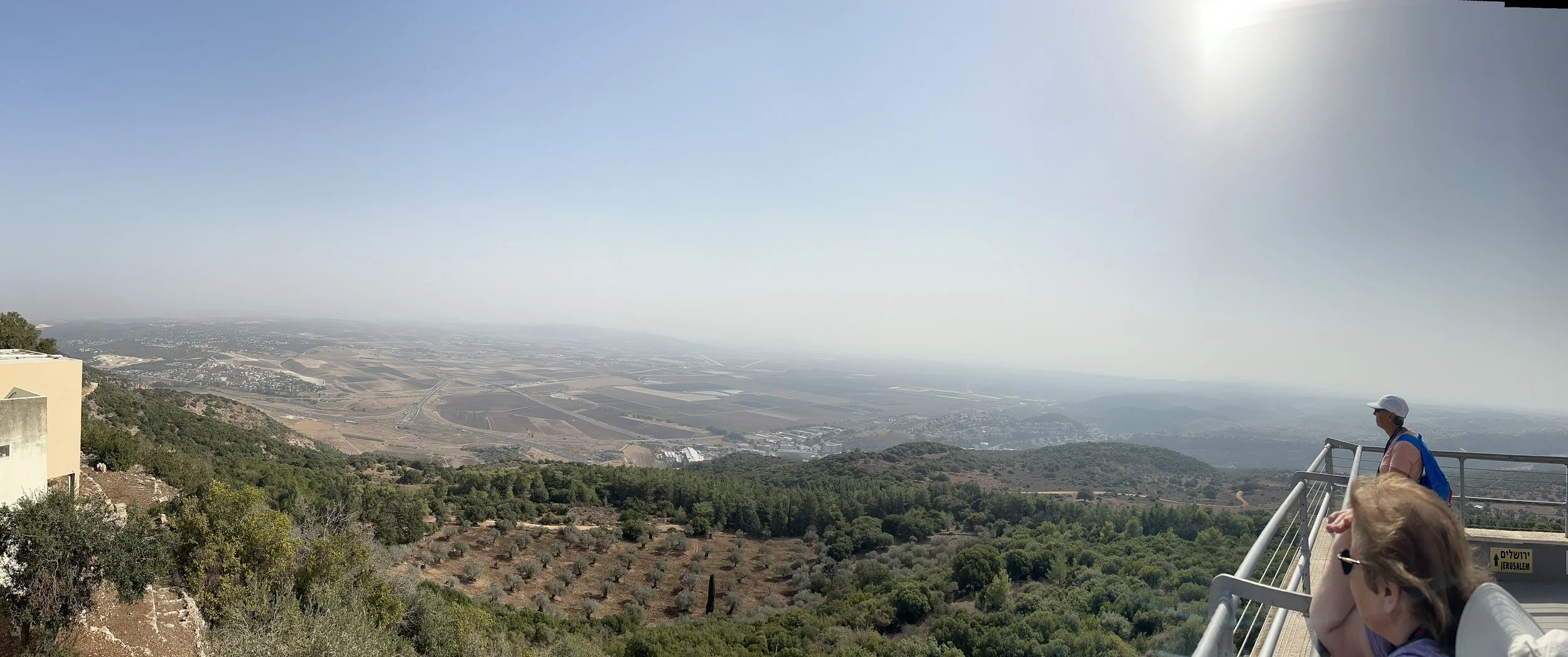 People standing on an observation deck overlooking a vast landscape with hills, farmland, and a distant city view on a clear day.