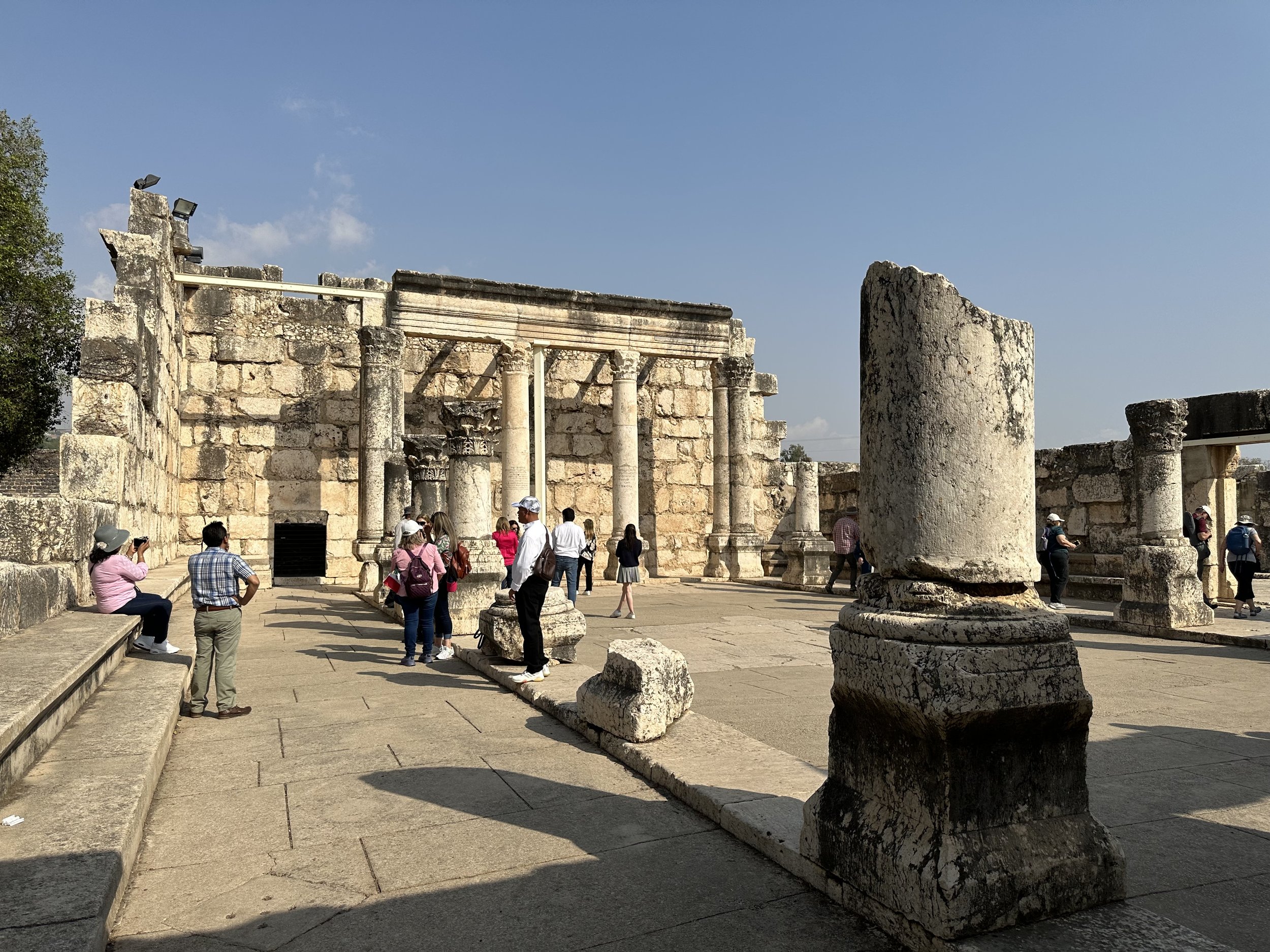 Tourists exploring ancient ruins with stone columns and walls, under a clear blue sky.