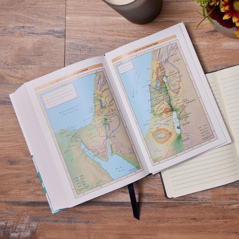 Open book displaying maps of ancient Israel, land of the twelve tribes, on a wooden table with a notebook, a cup, and a flower arrangement nearby.