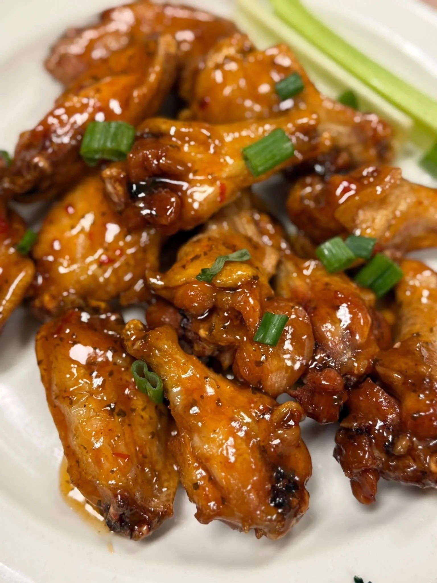 Close-up of glazed chicken wings garnished with chopped green onions on a white plate.