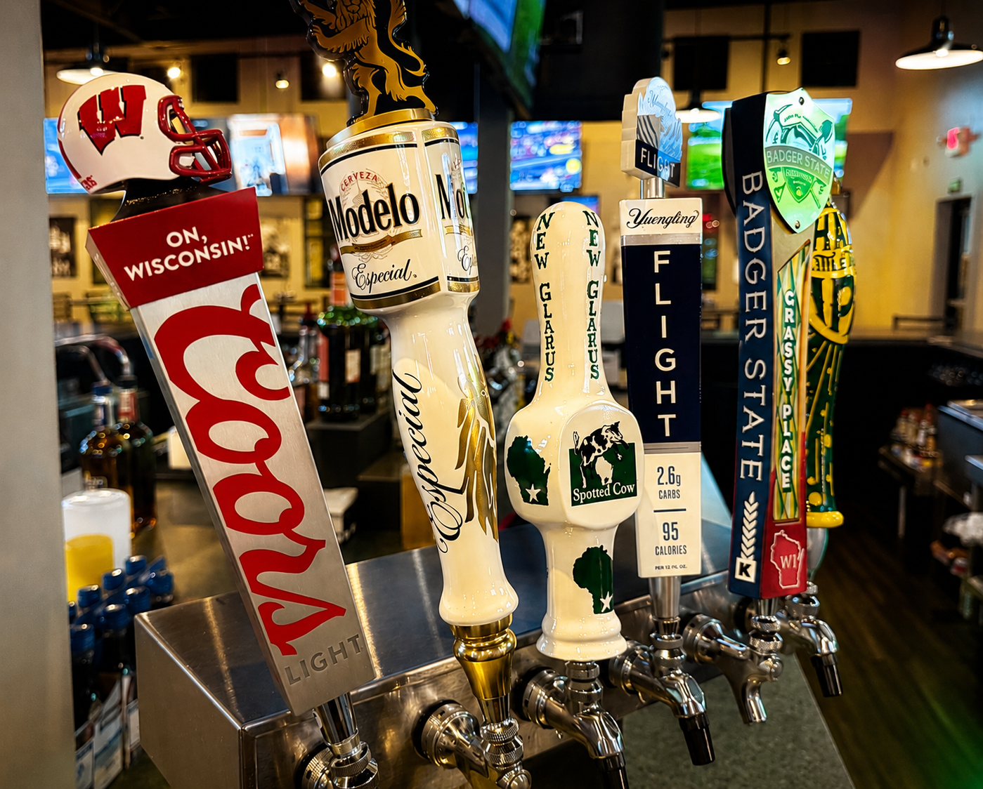 Beer tap handles with various team logos and designs displayed in a bar.
