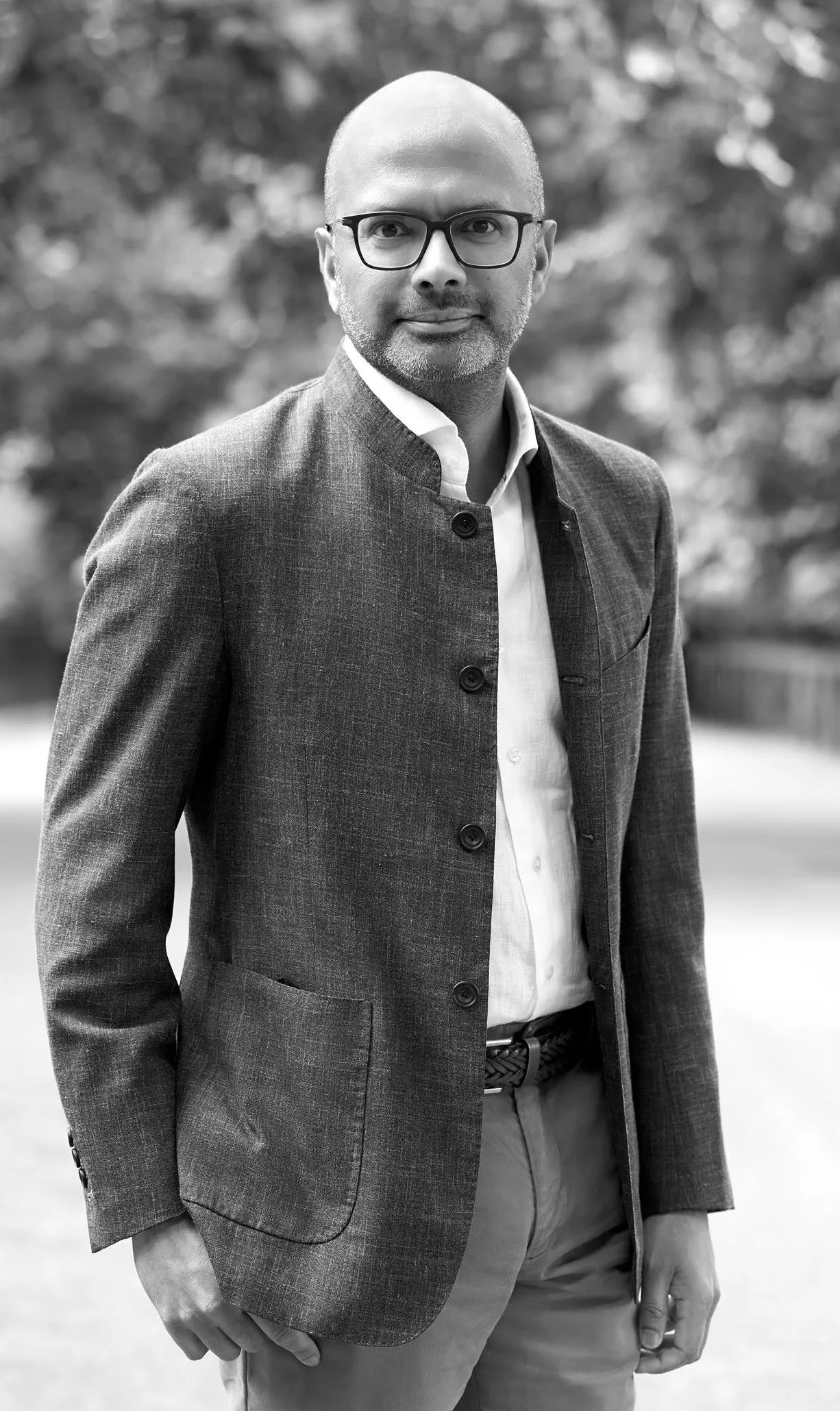 Black and white headshot of Supraj Rajagopalan with glasses and a slight smile against a blurred outdoor background.