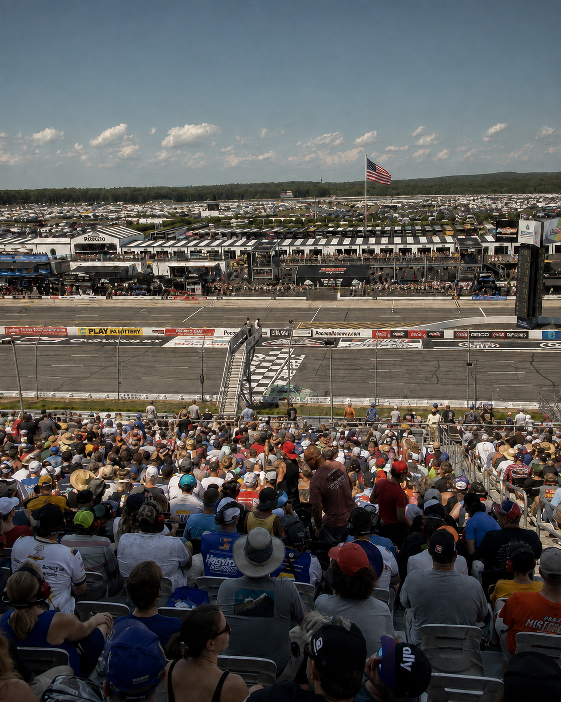 Crowd watching a NASCAR race at Pocono Raceway with the speedway and infield in the background.