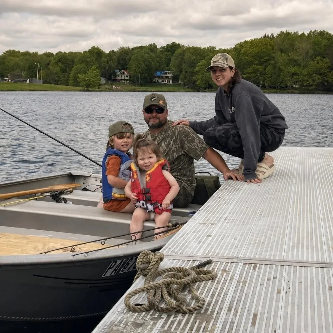 Family with children wearing life jackets beside a jon boat on the lake.