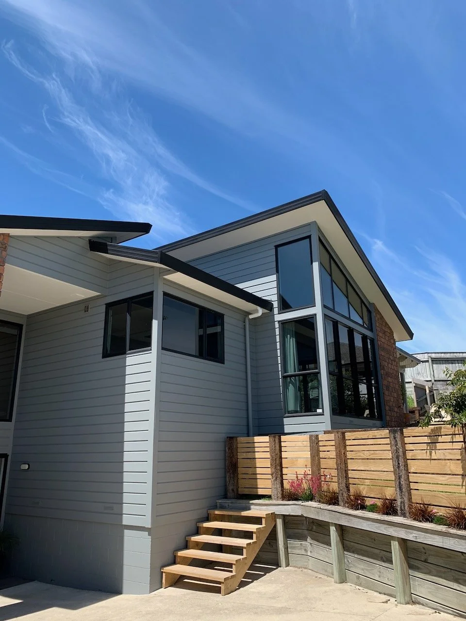 Modern house with gray siding, large glass windows, and a balcony under a blue sky.