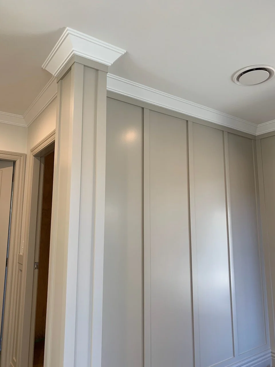Interior corner of a room with beige walls, white crown molding, and paneled wall with vertical strips.