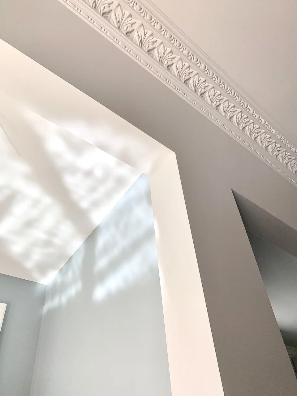 Close-up of ornate crown molding on ceiling with sunlight casting shadows.