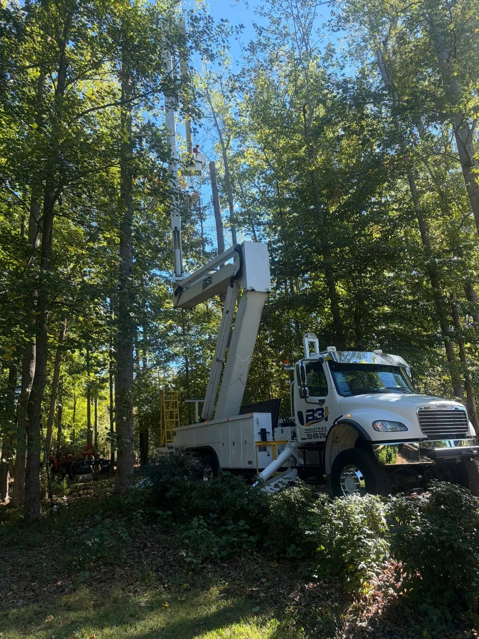 White utility bucket truck with an elevated worker platform among trees.