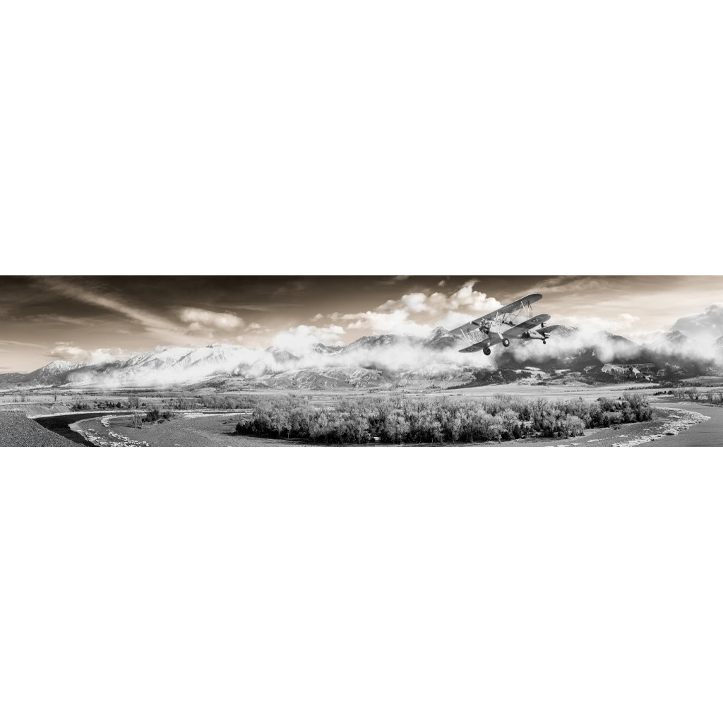 Black-and-white panoramic view of a biplane flying above Paradise Valley, Montana, with the Yellowstone River and mountains below, photographed by Tom Lance.